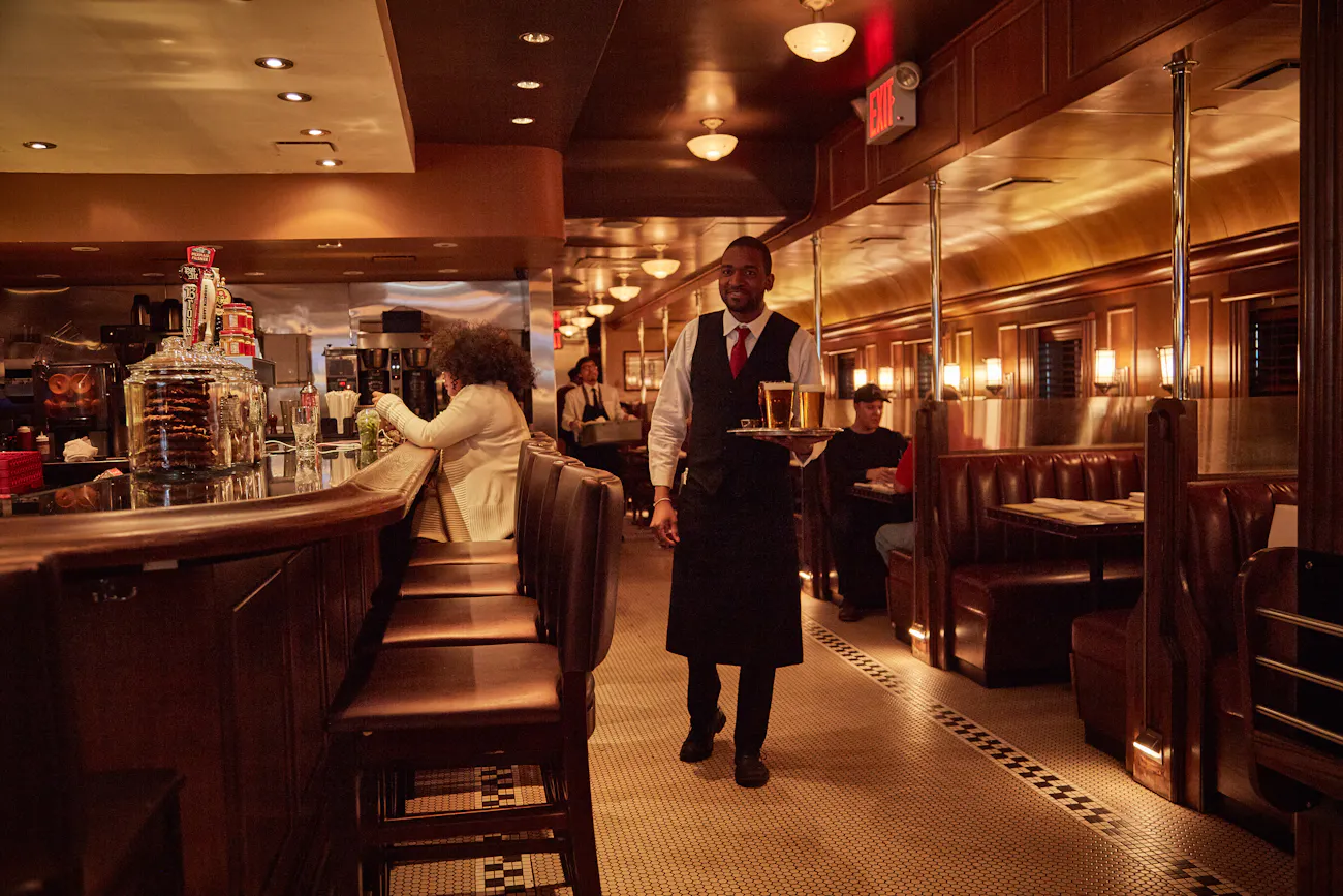 A server carries a tray through the warm, wood-panelled Brooklyn Diner dining room