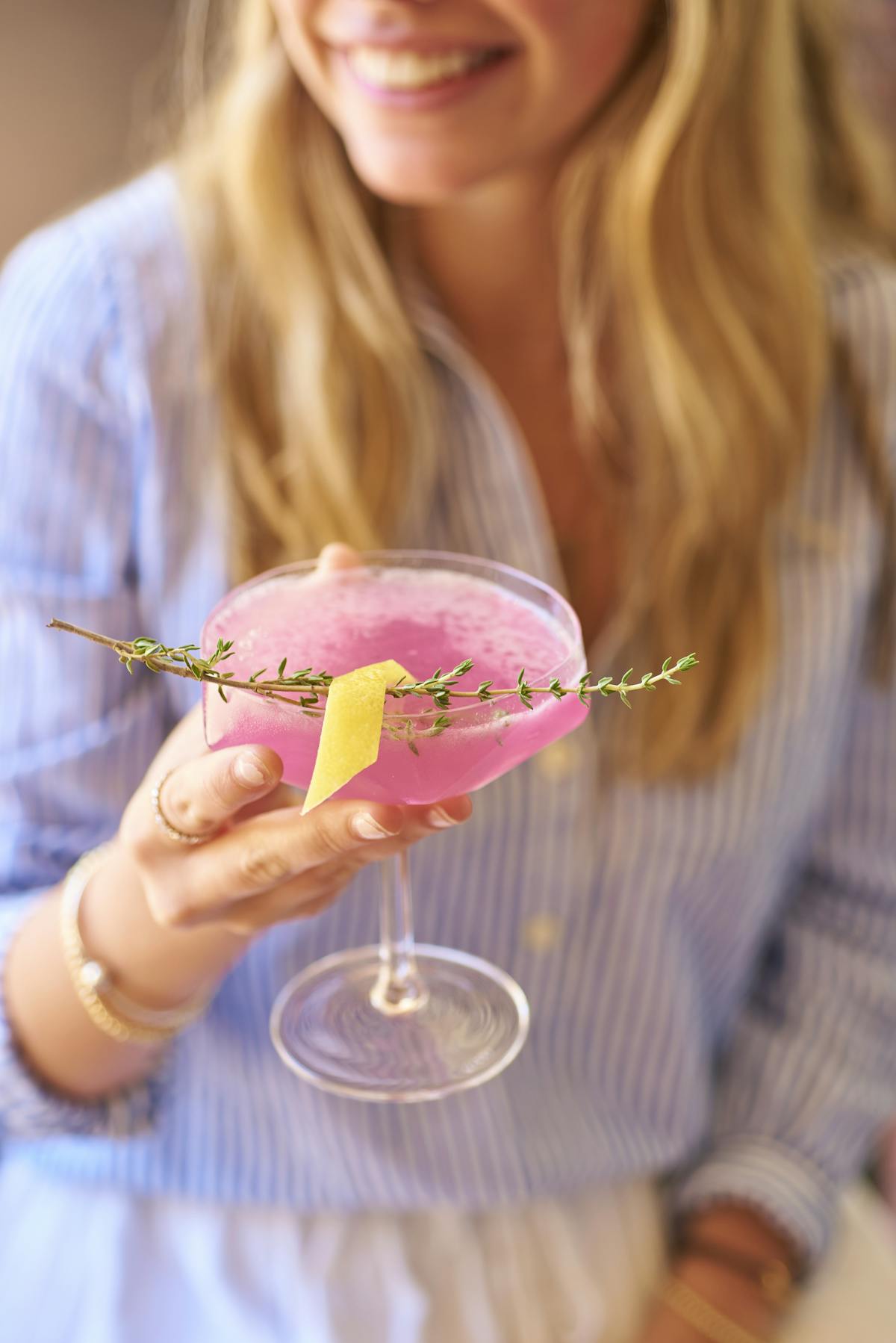 a woman holding a coupe glass with a pink cocktail