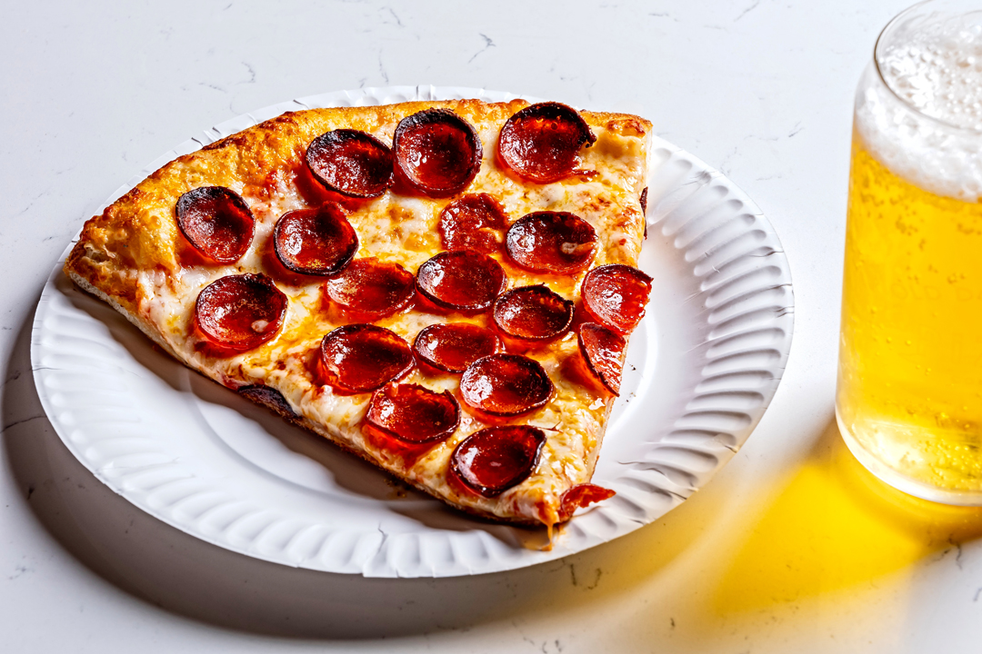 a slice of pepperoni pizza on a plate with a cold beer next to it