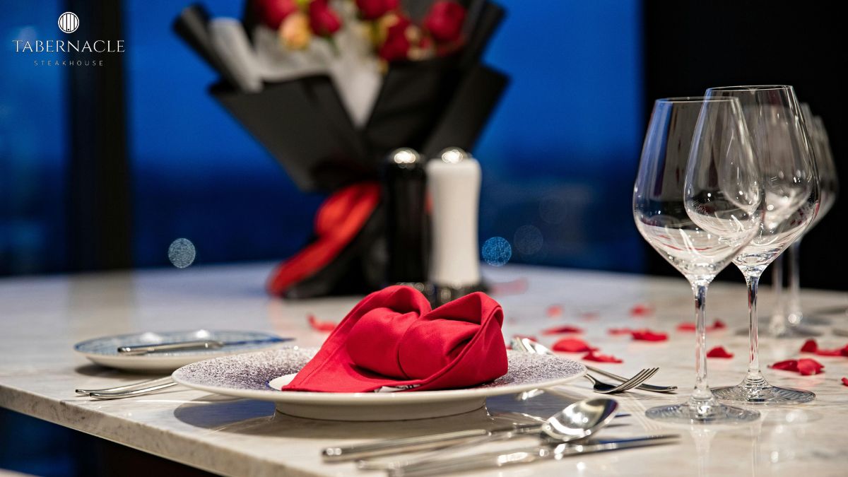 Romantic table setting at Tabernacle Steakhouse for a kosher anniversary dinner in NYC, with red roses, wine glasses, and rose petals