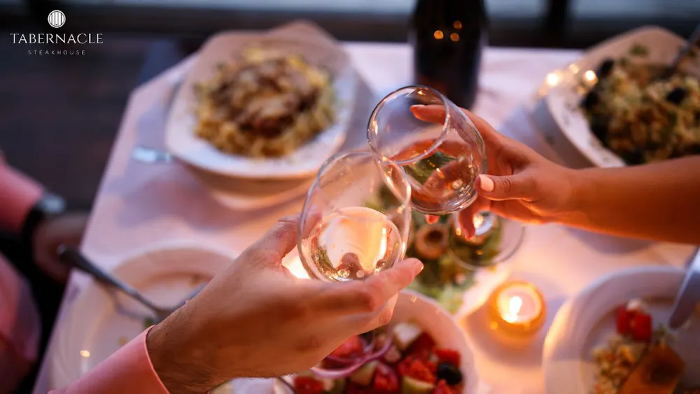 Couple toasting wine glasses over a candlelit kosher dinner table at Tabernacle Steakhouse in NYC