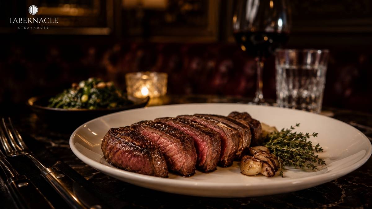Sliced steak on a white plate with thyme, roasted garlic, and red wine