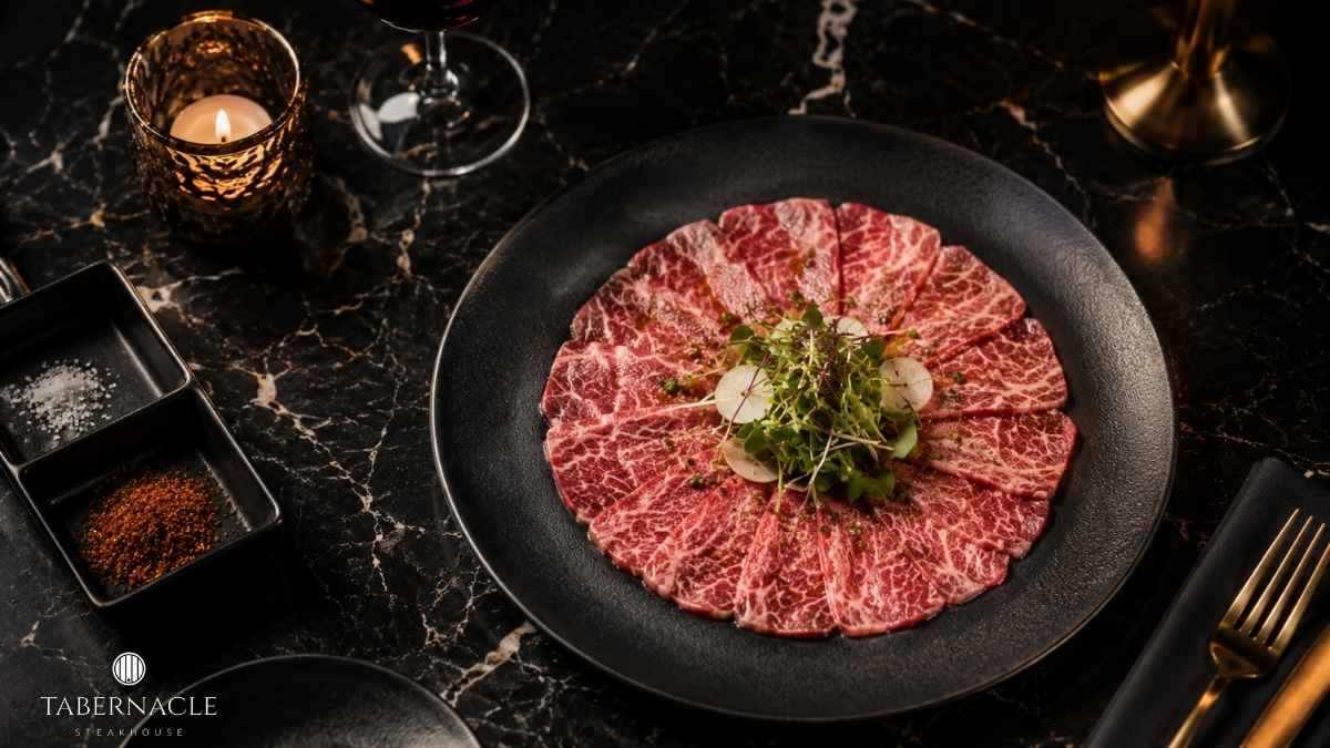 Wagyu carpaccio plated with microgreens and seasoning on marble table