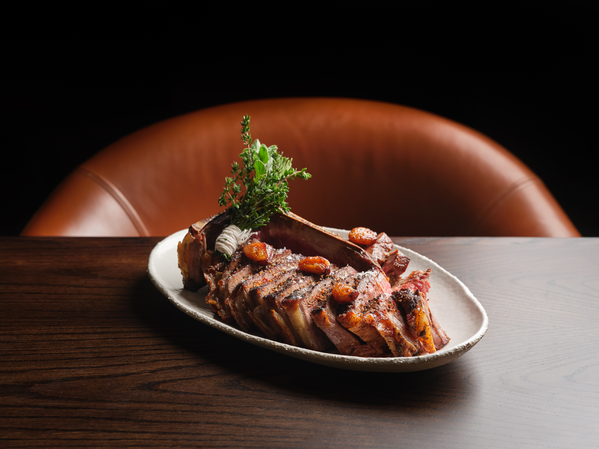 a T-bone steak on a white plate placed on a wooden table.