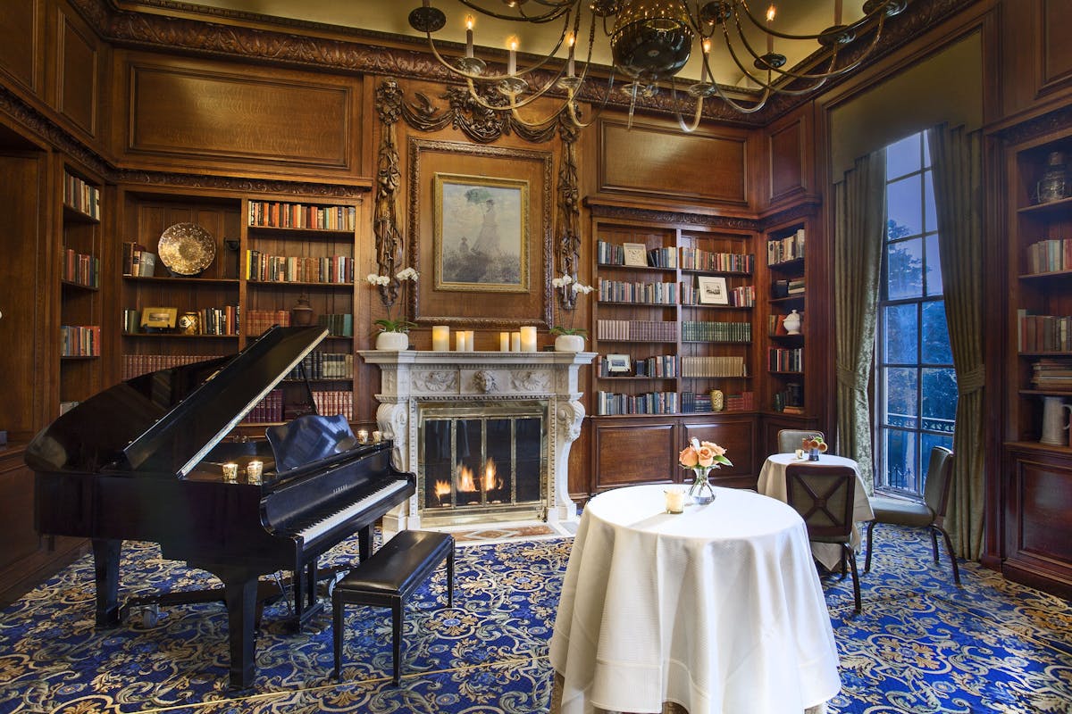 a room with a table, piano, and fireplace