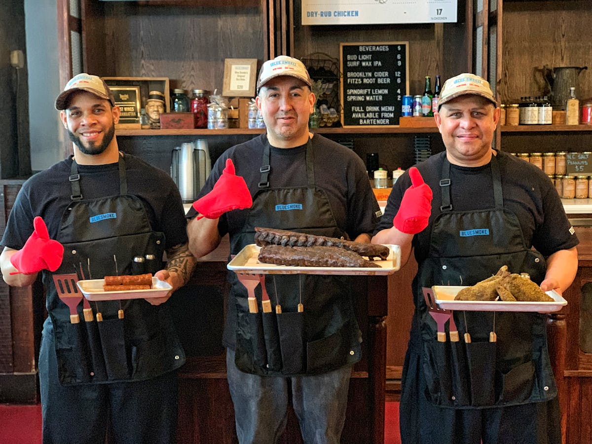 men wearing Blue Smoke aprons, holding different barbecued meat