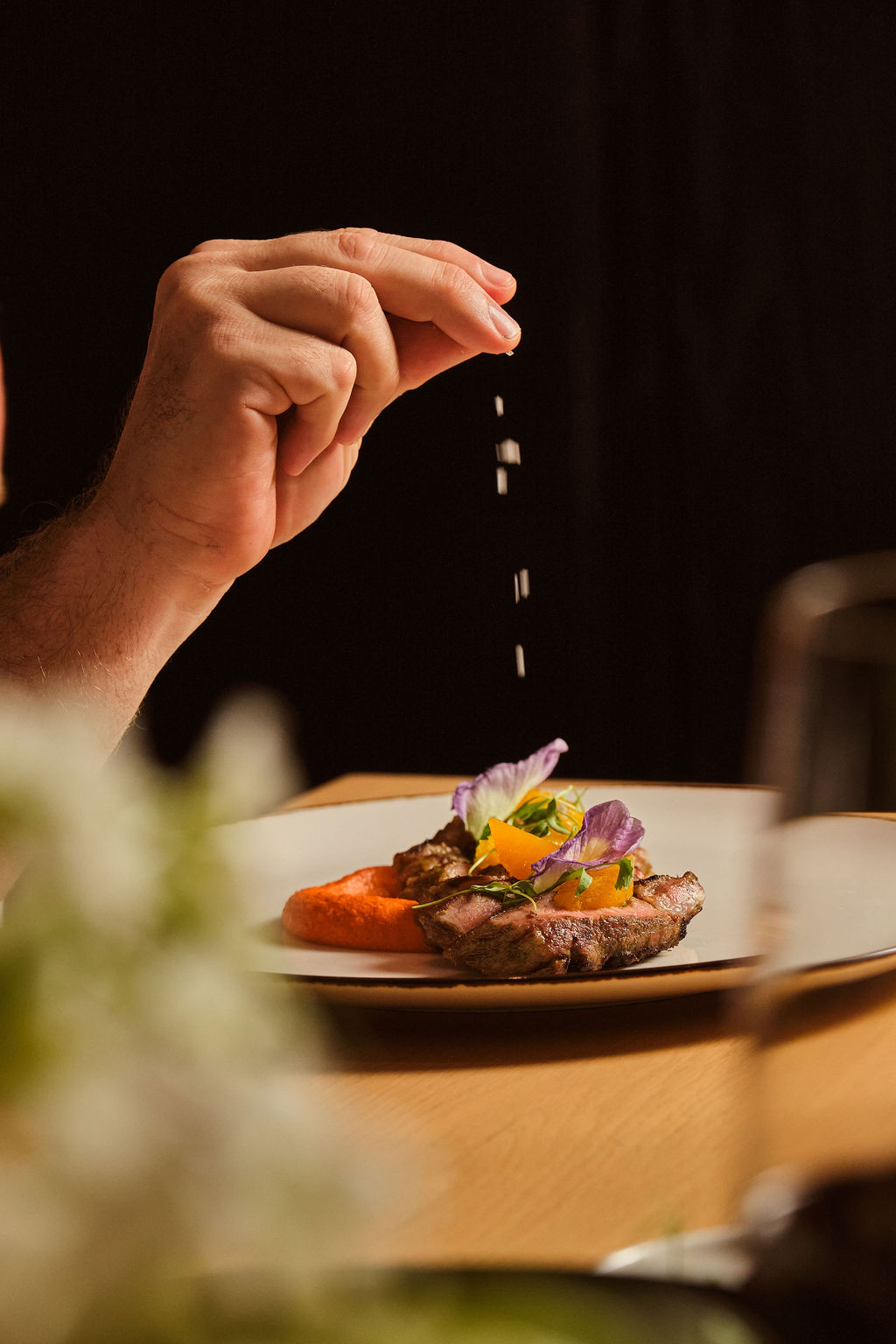 a hand sprinkling salt on a plate of food