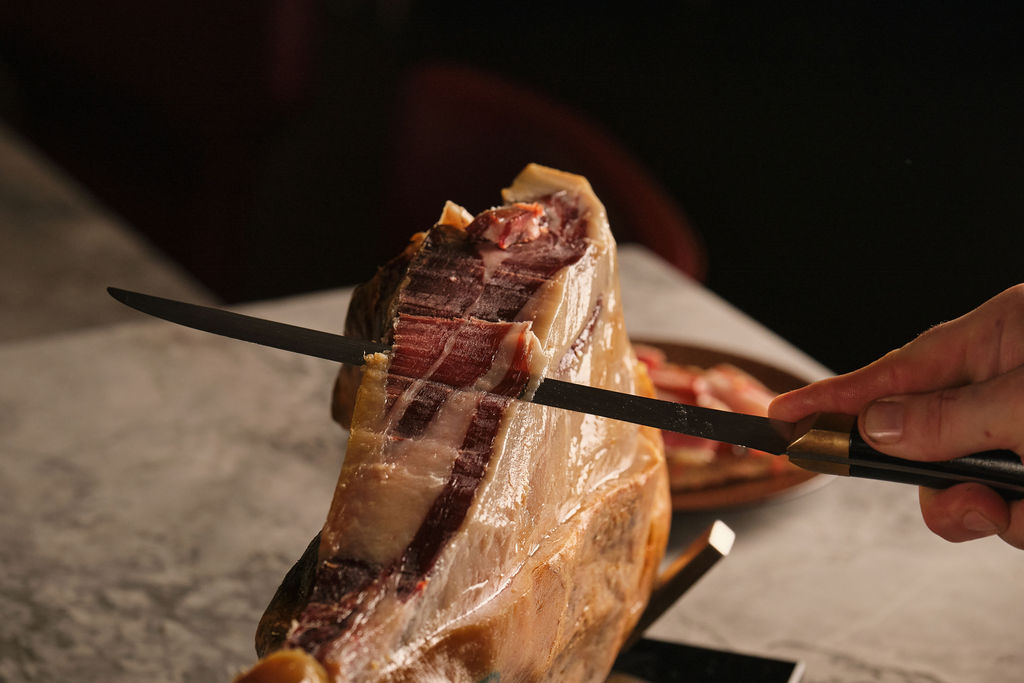a hand holding a fork and knife on a cutting board with a cake