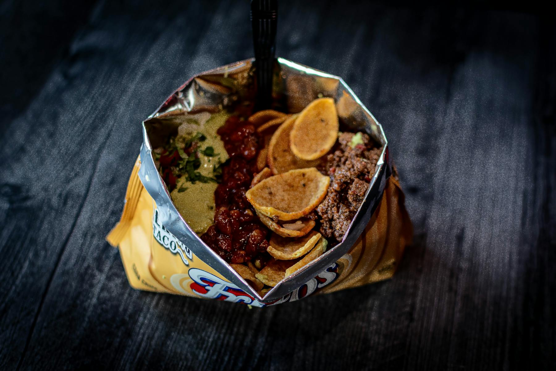 A bag of Fritos loaded with beans, guacamole, crema, and barbacoa