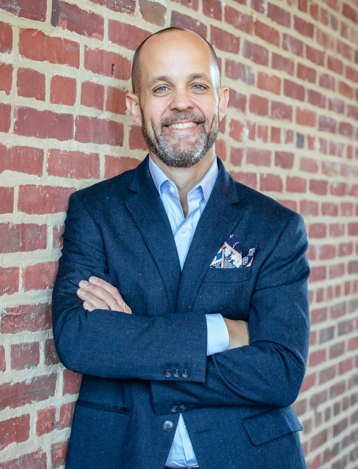 a man wearing a suit and tie standing next to a brick wall