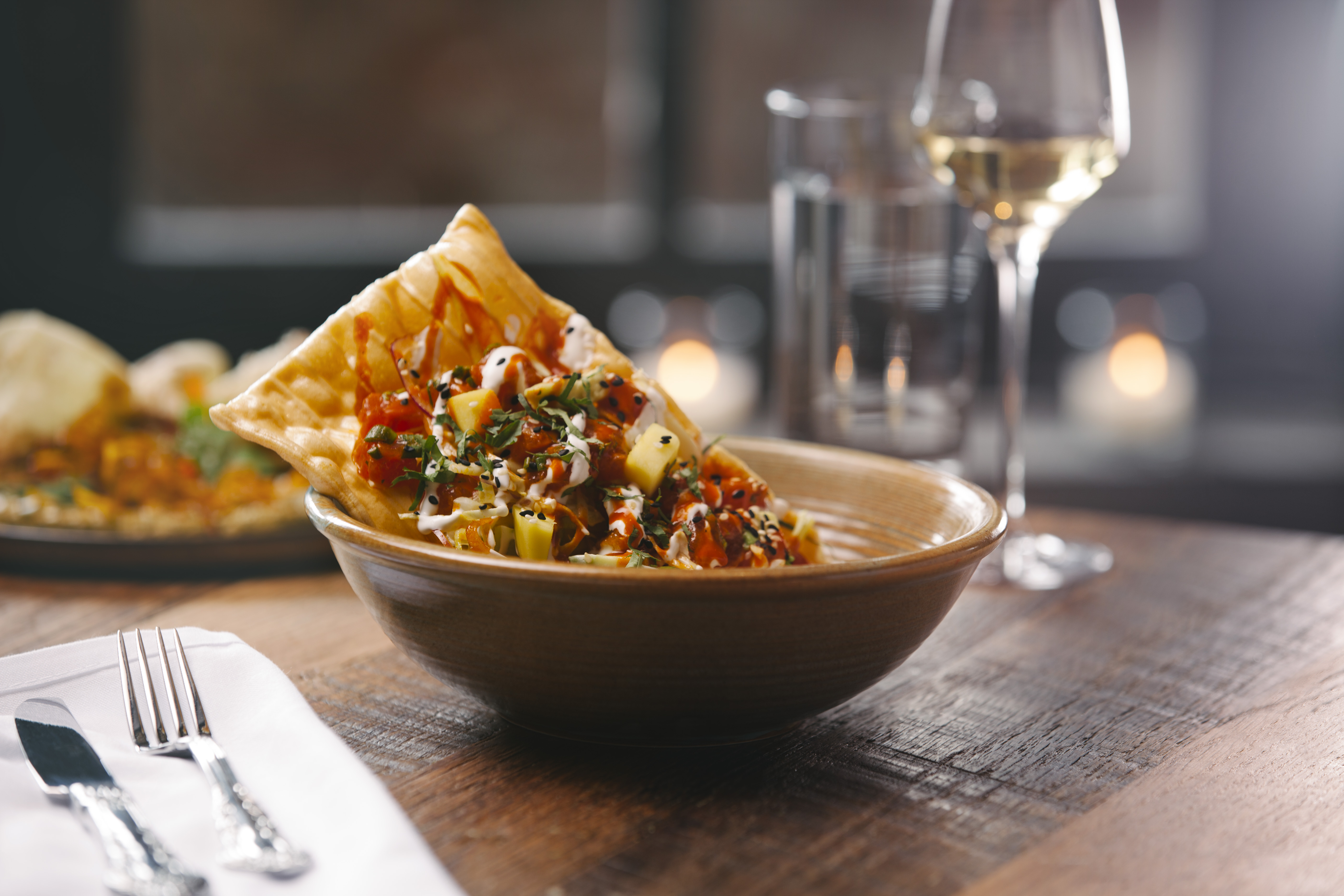 a bowl of food on a plate next to a glass of wine