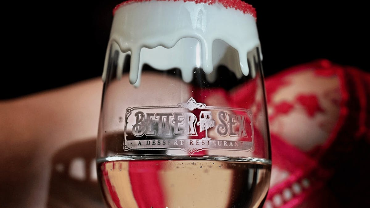 closeup of a glass of sparkling white wine with the logo for Better Than Sex - A Dessert Restaurant