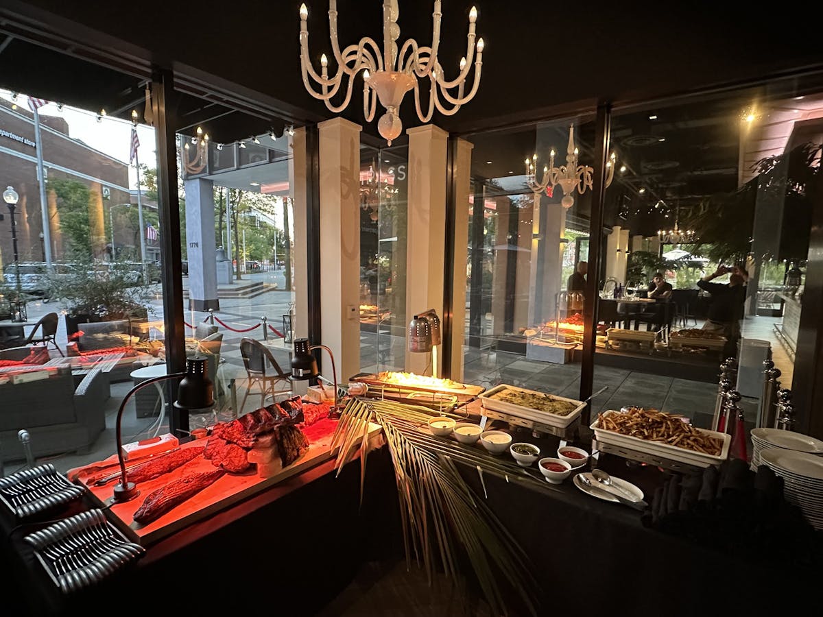 A buffet table laden with food, illuminated by a chandelier, set against a backdrop of a large window.