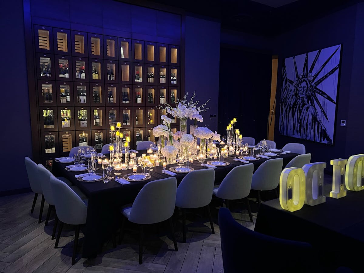 A table surrounded by white chairs, featuring a prominent sign displaying event details
