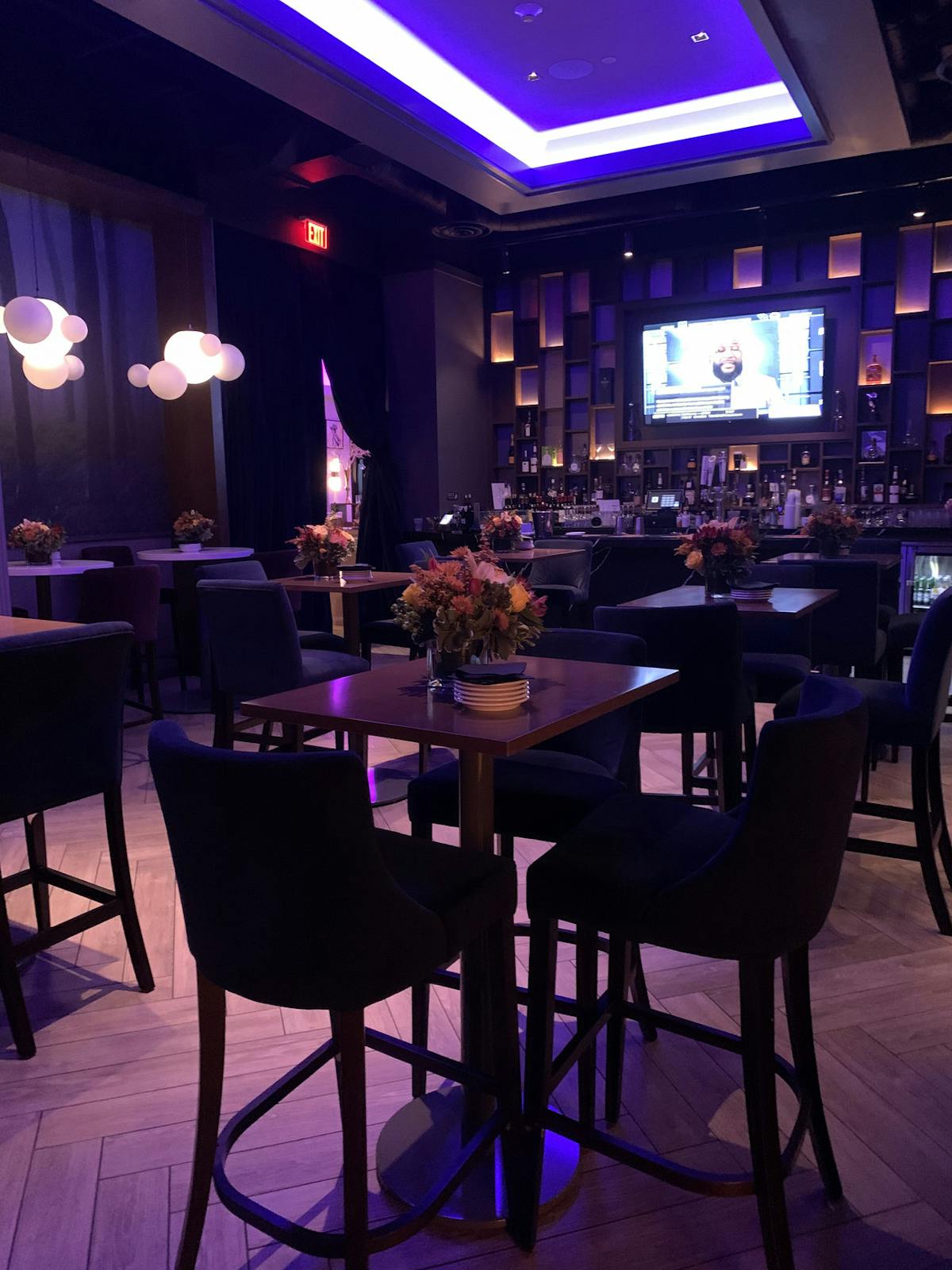 A stylish bar illuminated by purple lighting, featuring modern chairs arranged for a vibrant atmosphere.