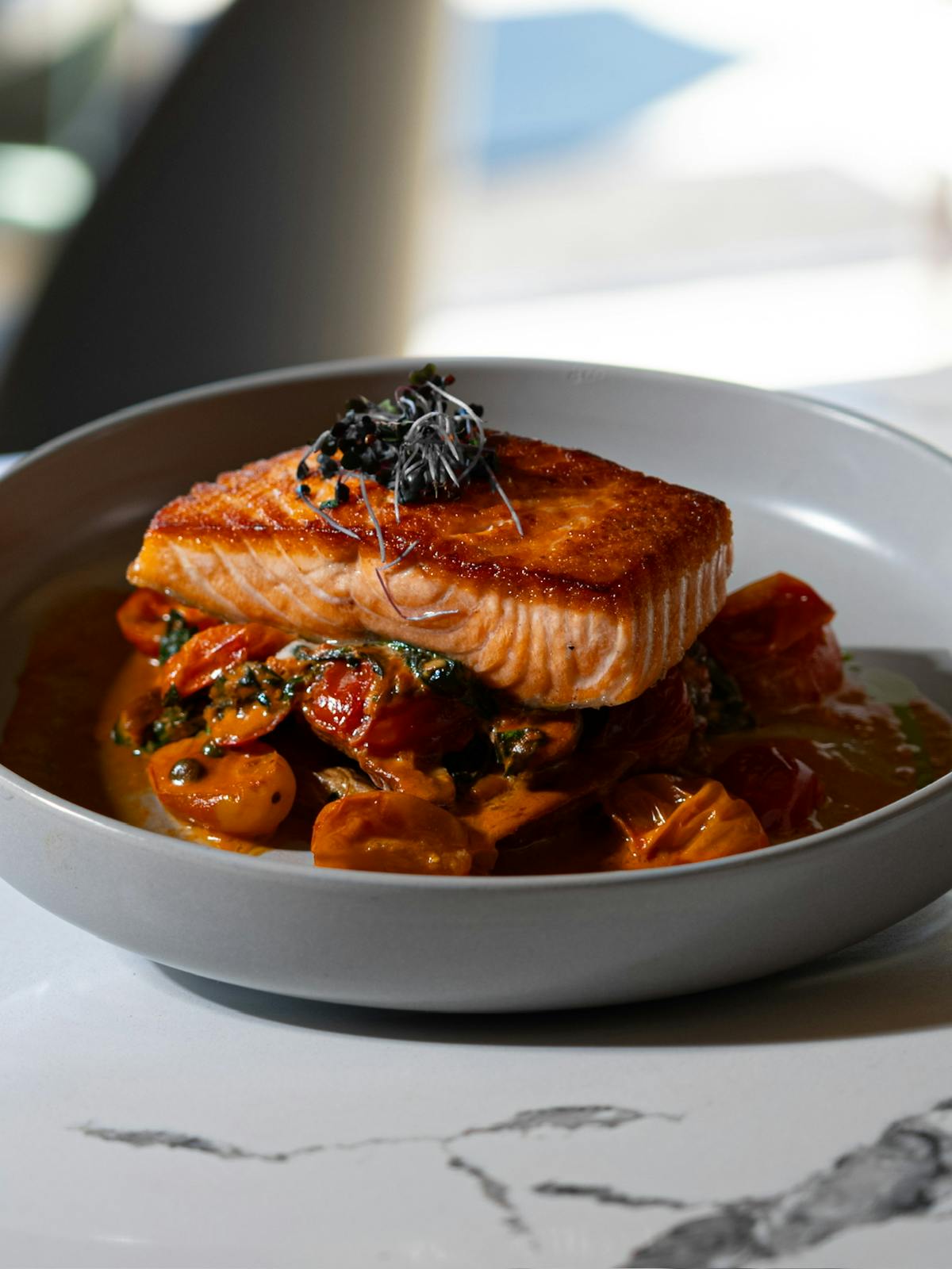 A plate of salmon with tomatoes and sauce elegantly arranged on a dining table.