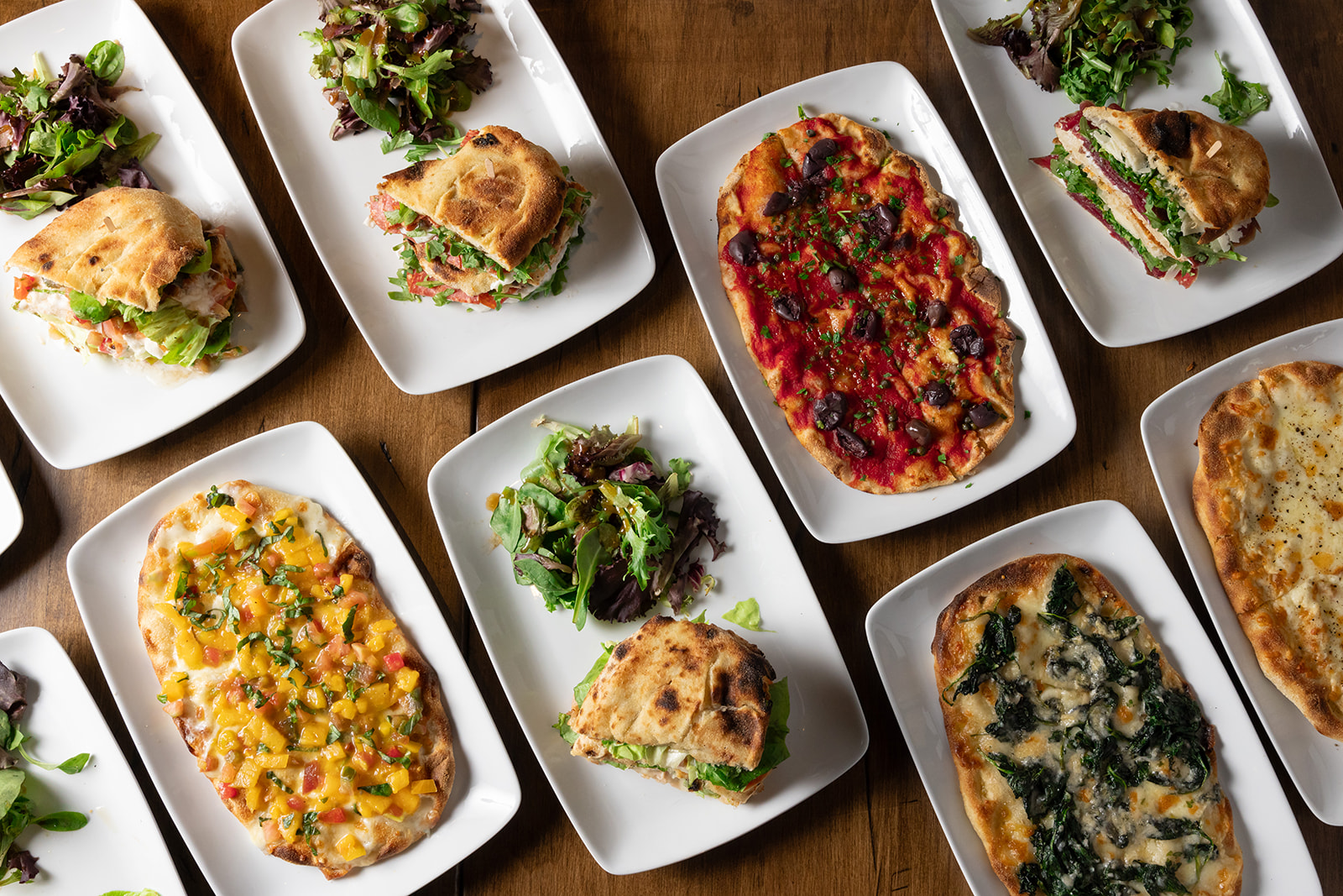 a table full of Pinsas, paninis, and greens salads