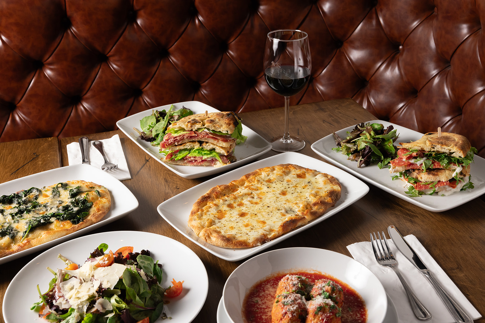 a table with pinsas, red wine, paninis and a glass of red wine