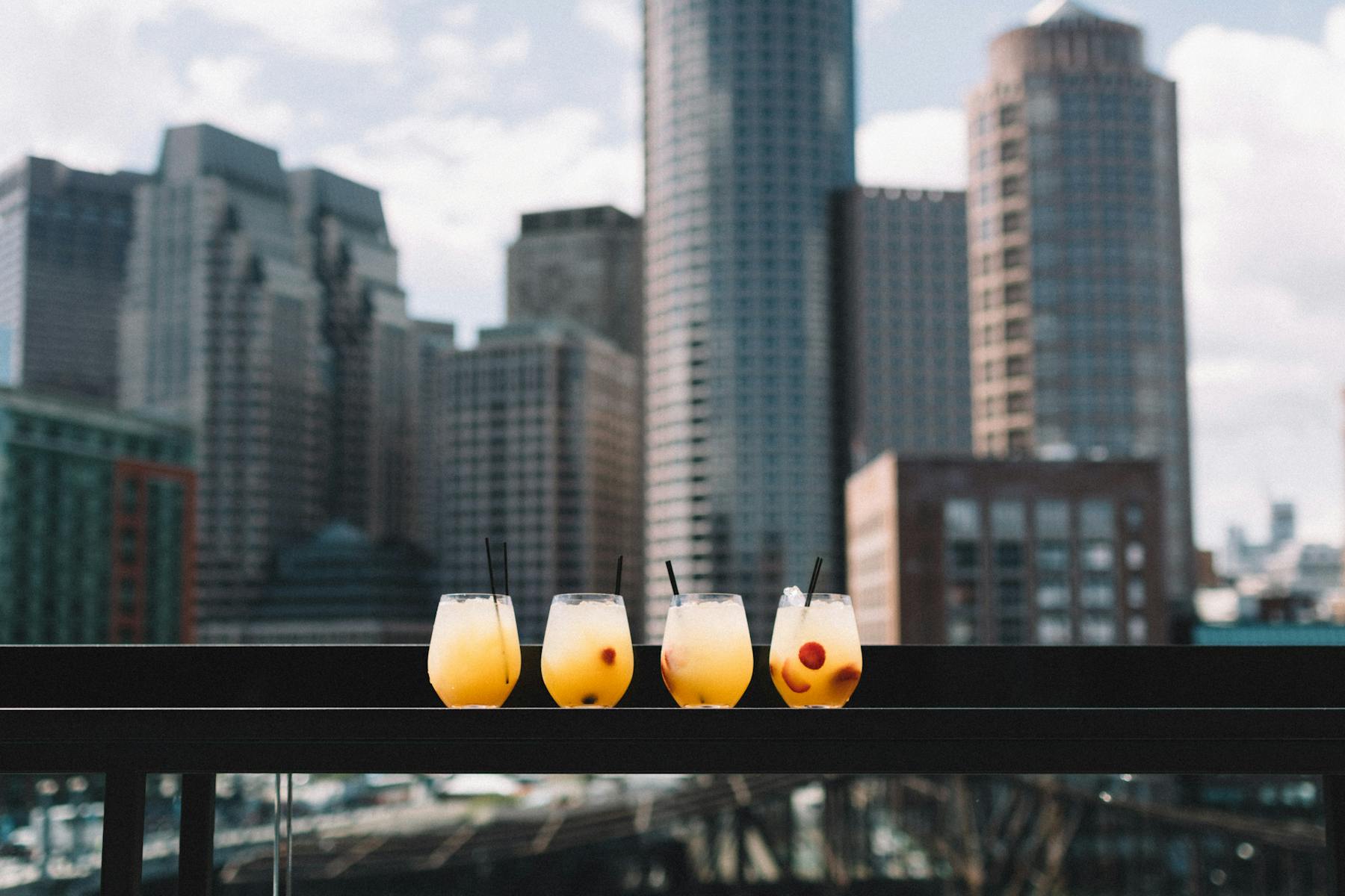 four glasses of orange drink with a tall building in a city as a background