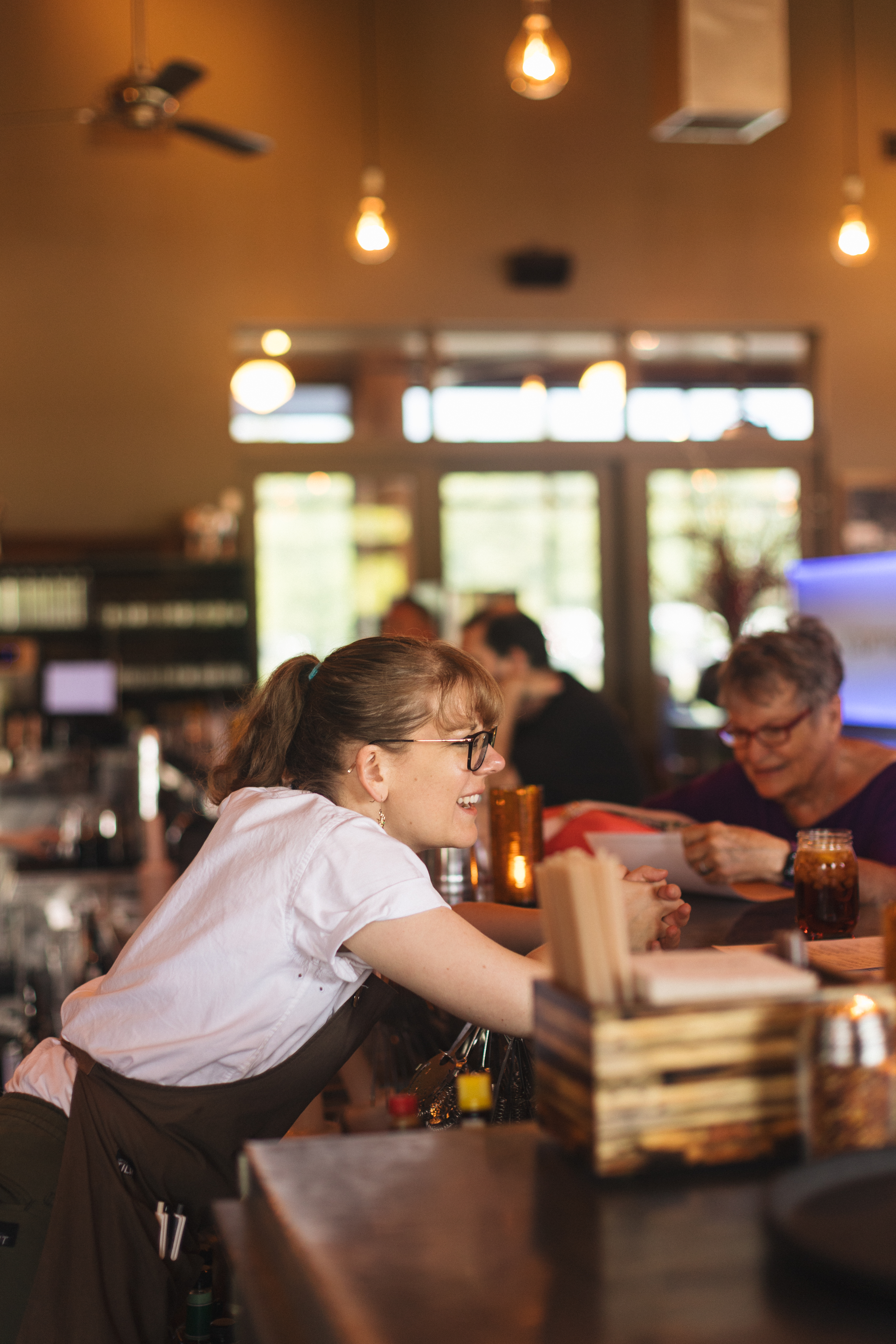 A Firefly Grill server leaning over the bar, smiling with guests