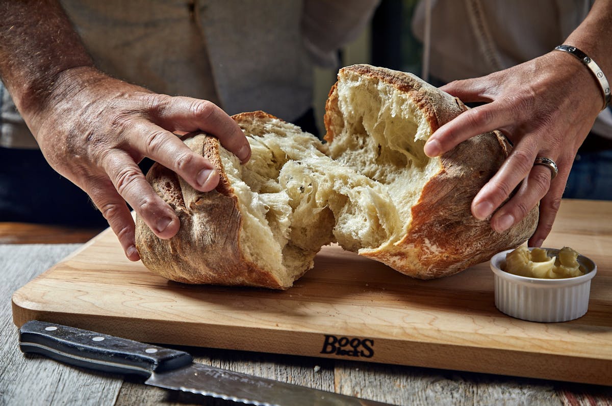 a person holding a piece of bread on a cutting board