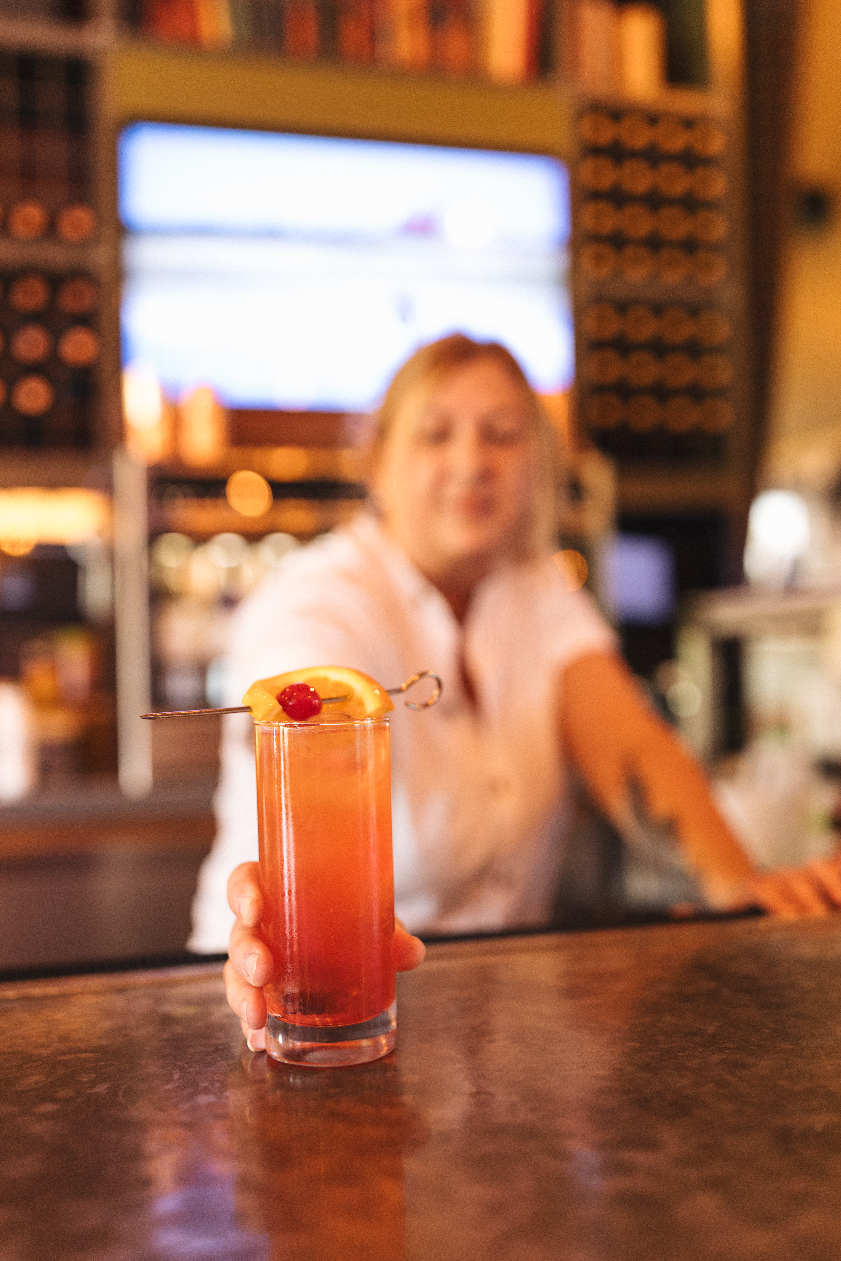 a person holding a glass of liquid with a slice of orange and cherry on it