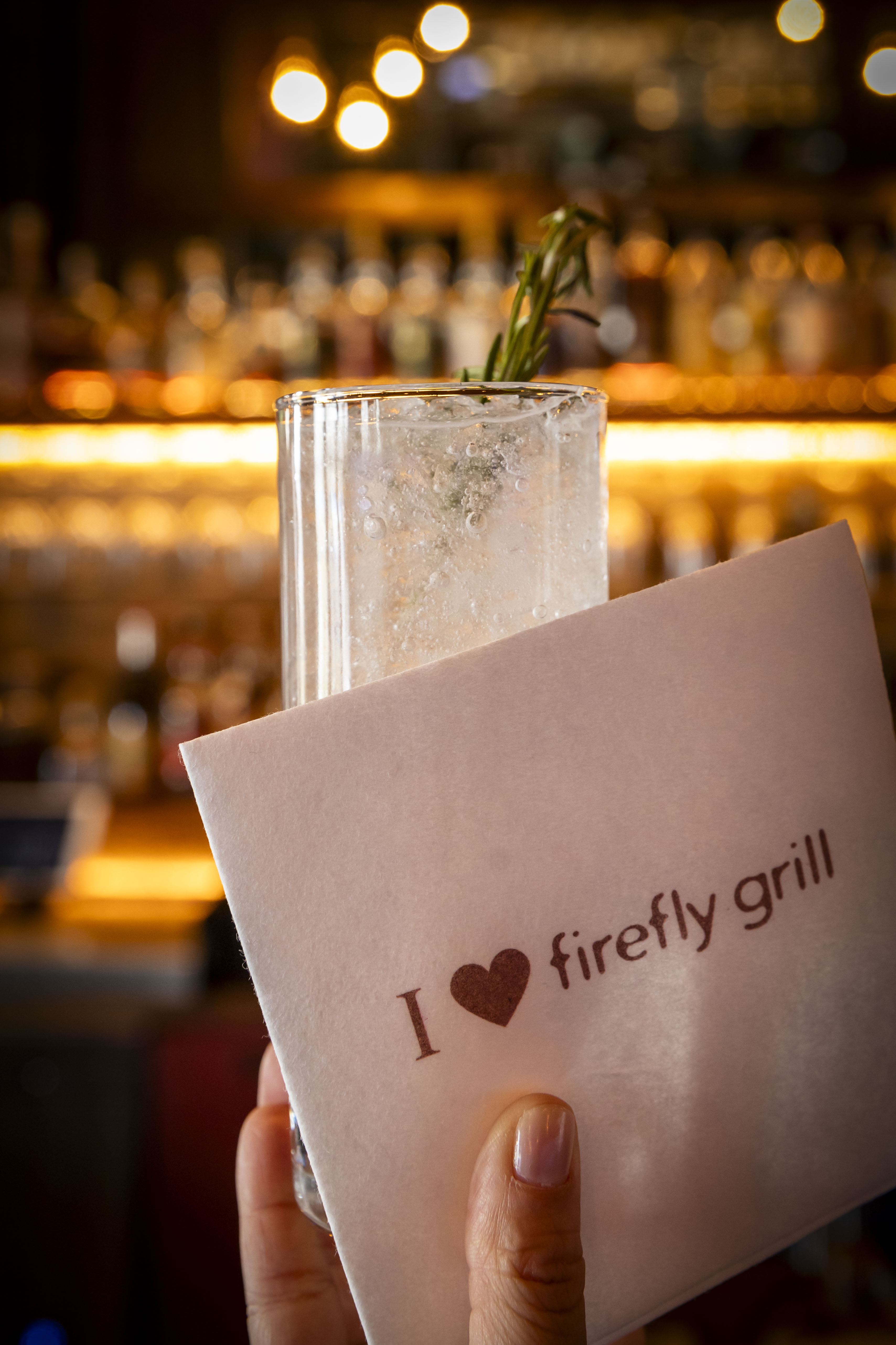 a hand holding a napkin with a drink and a rosemary sprig