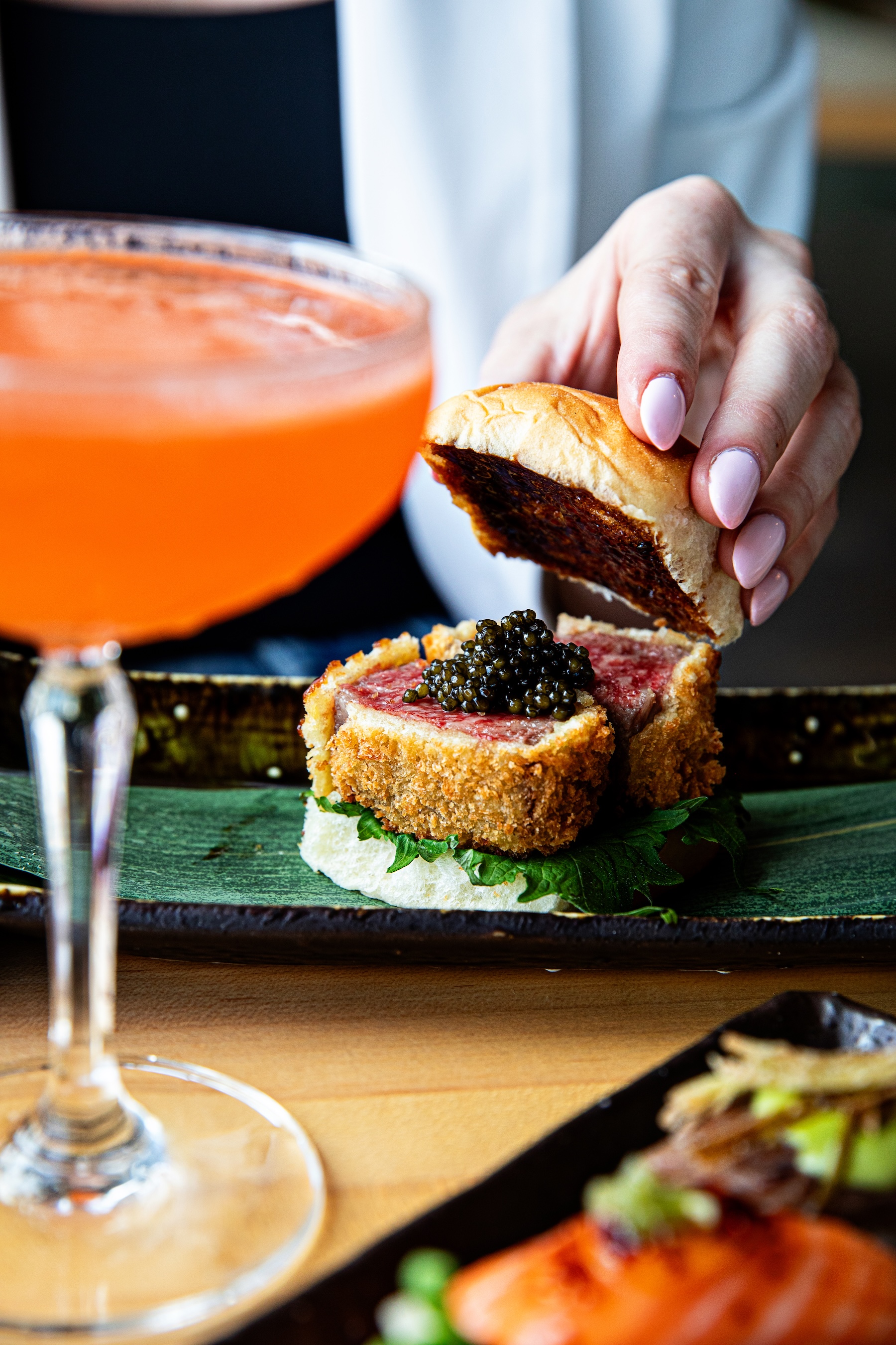 a hand holding a piece of meat on a plate with a drink
