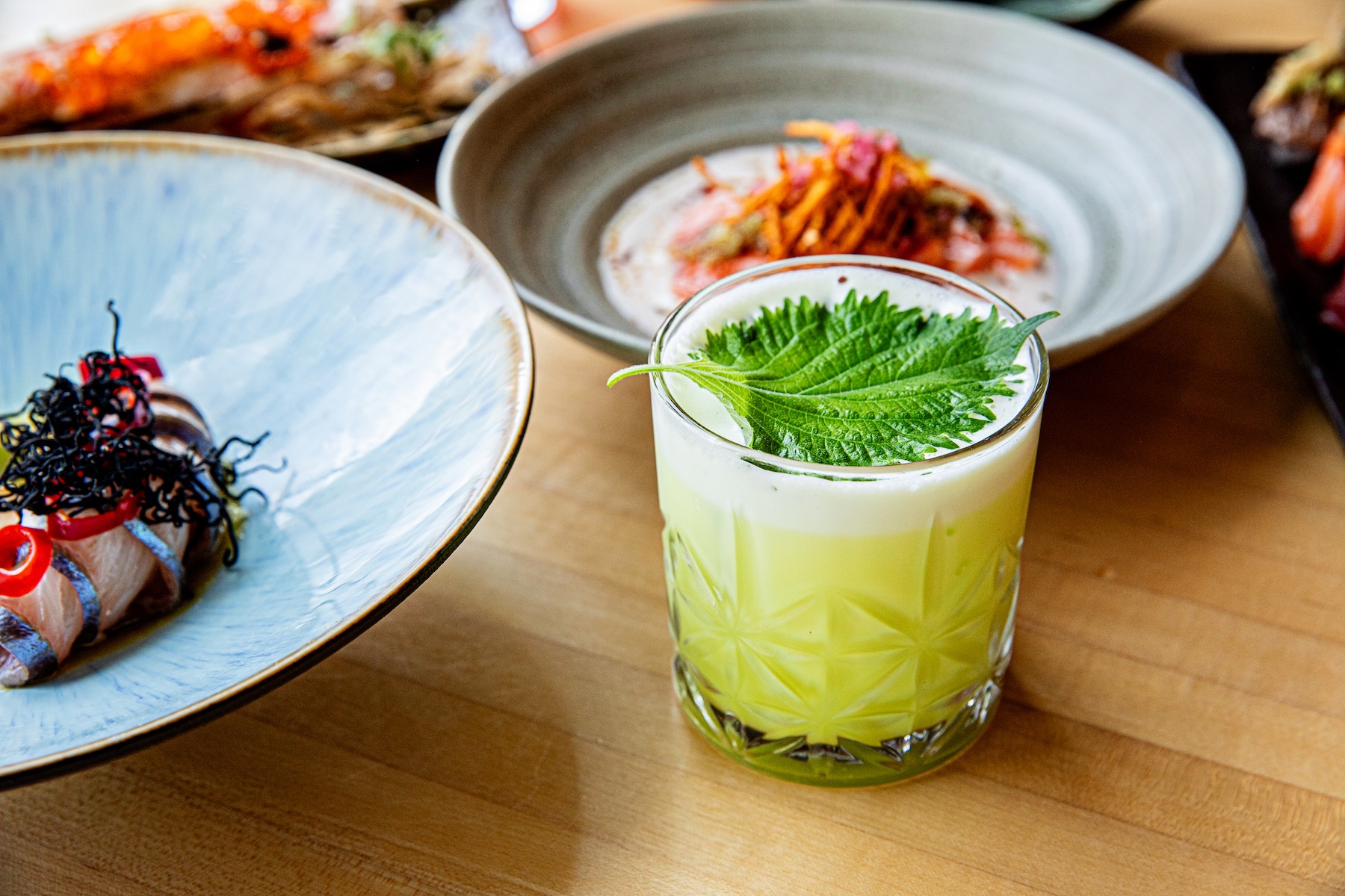 a glass with a green liquid and a leaf on top of it
