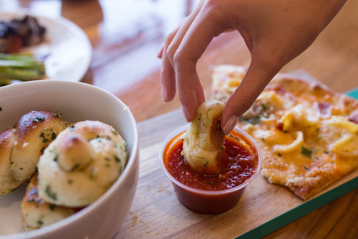 a hand submerging a piece of food on a sauce