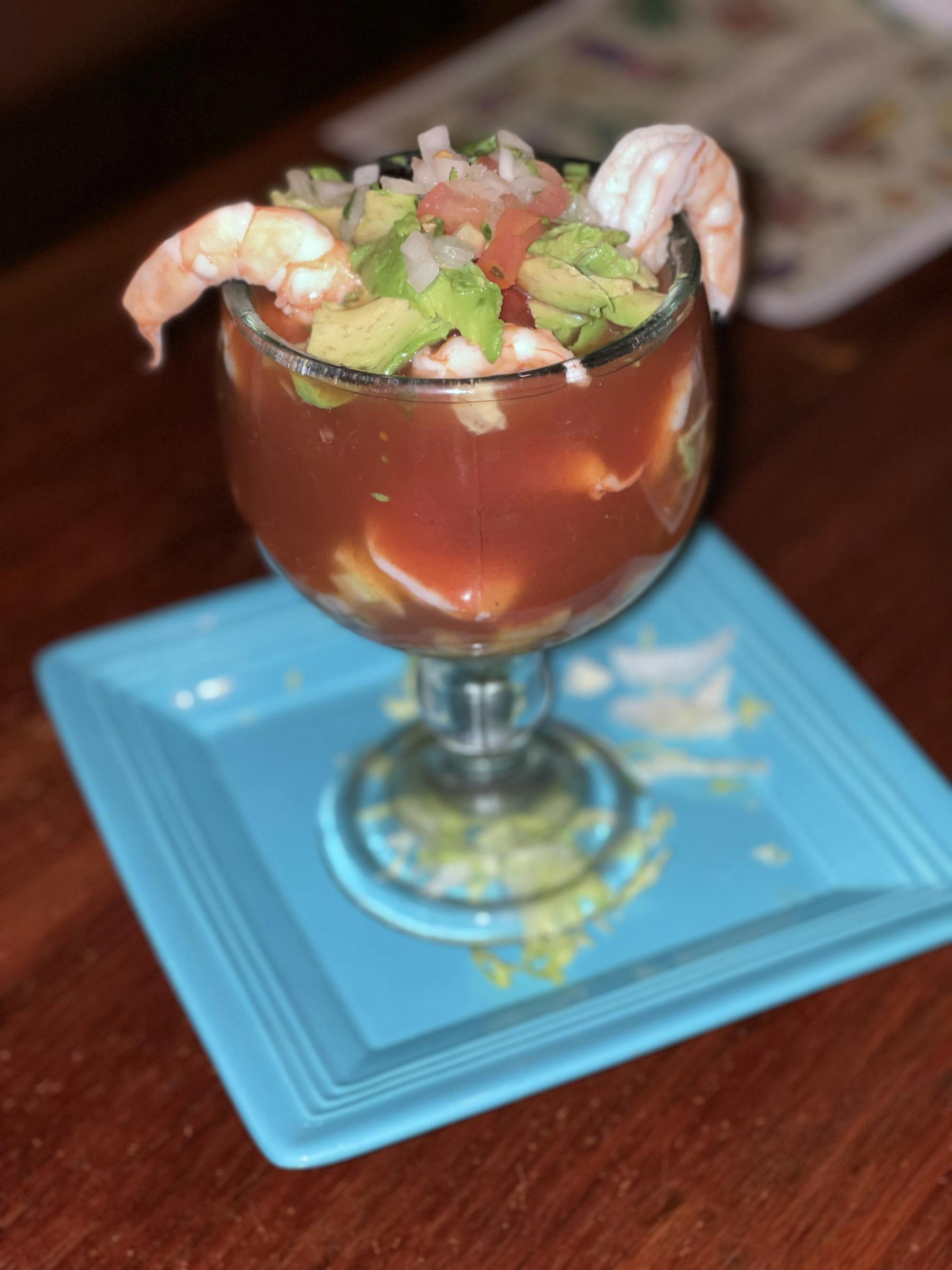a glass filled with shrimp cocktail sitting on top of a wooden table