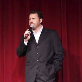 a man in a suit standing in front of a red curtain