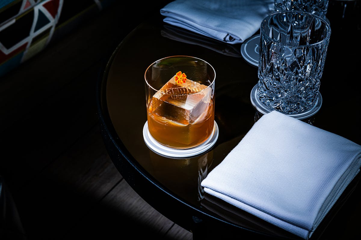 cocktail with an ice cube that reads barmini on a table