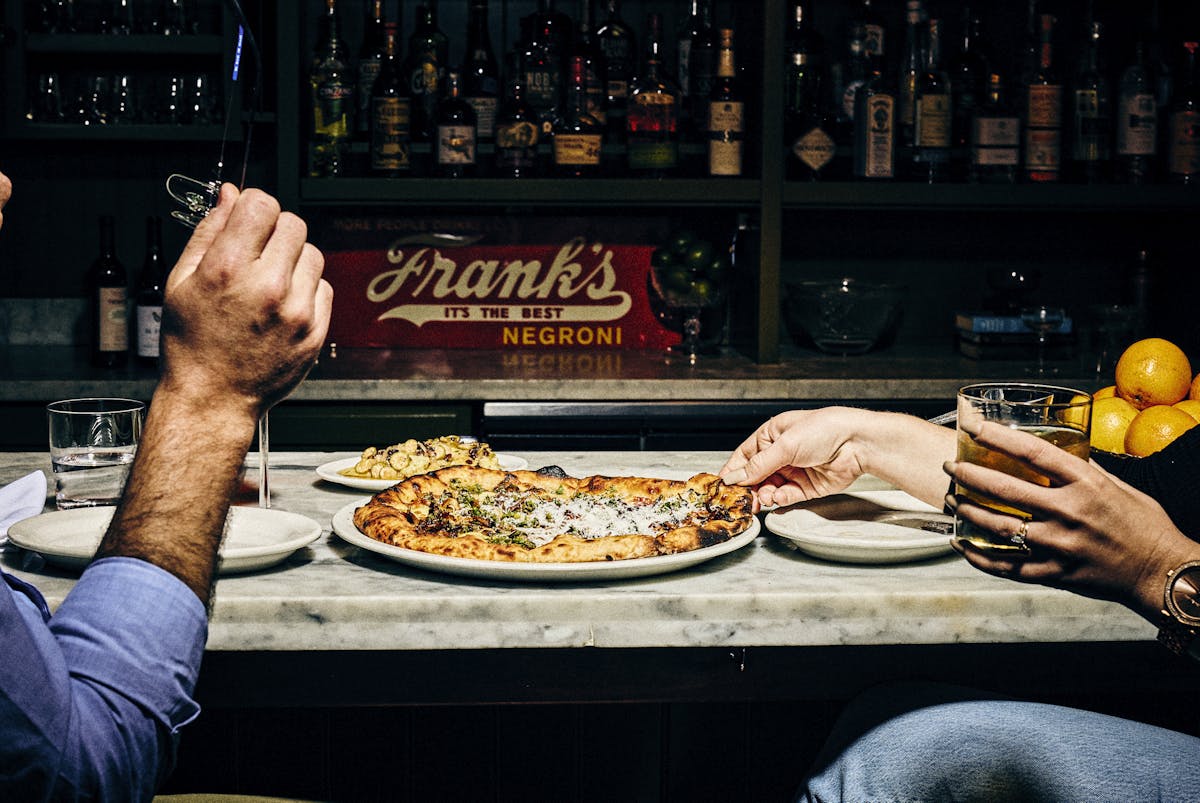 guests sitting at ciccio's bar, grabbing slices of pizza