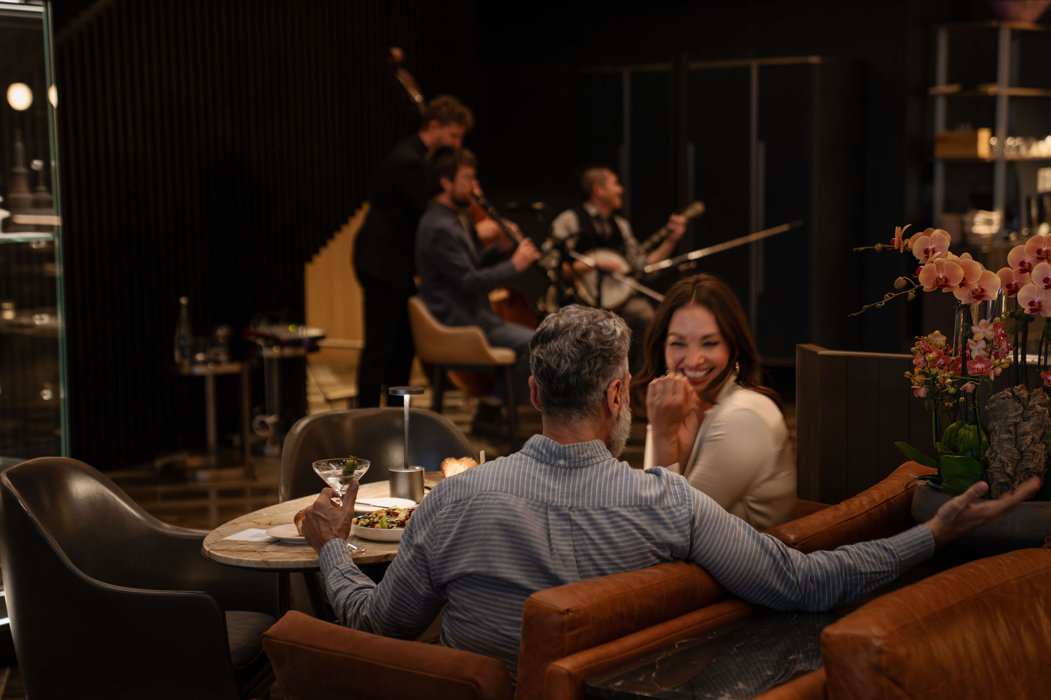 A couple enjoys a meal in a restaurant while a live band performs in the background, creating a lively atmosphere