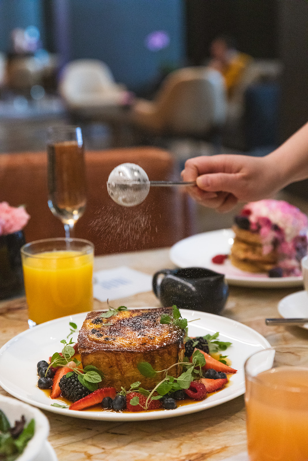 A person serves food on a table, accompanied by a glass of juice, creating a welcoming dining atmosphere
