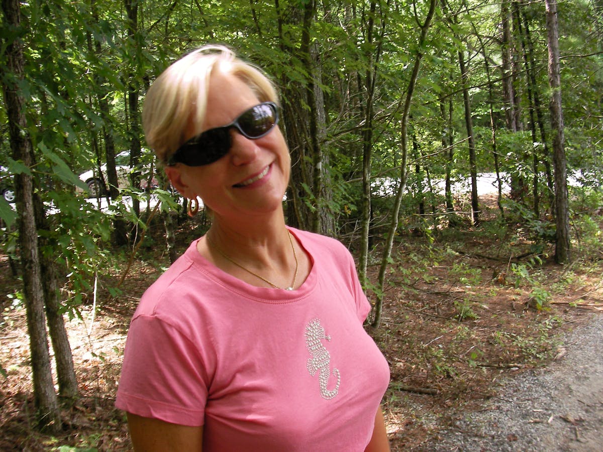 a woman wearing sunglasses standing in front of a forest