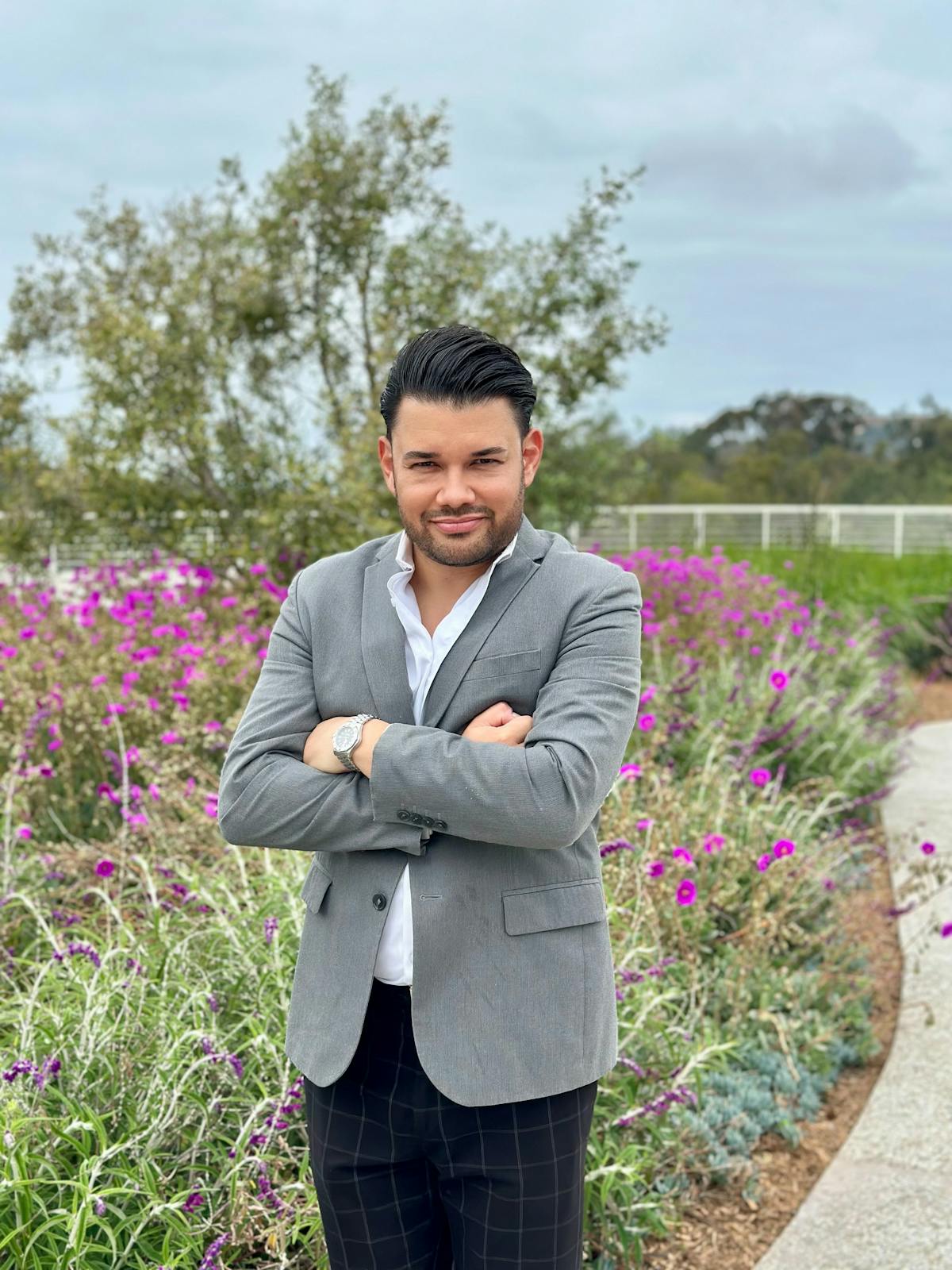 Image of a bearded man in a gray blazer standing in front of a field of purple wildflowers