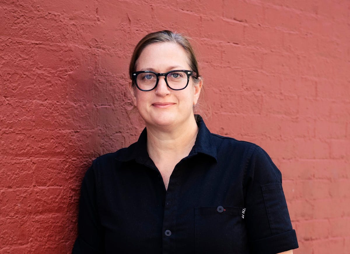 a person wearing glasses and standing in front of a brick wall