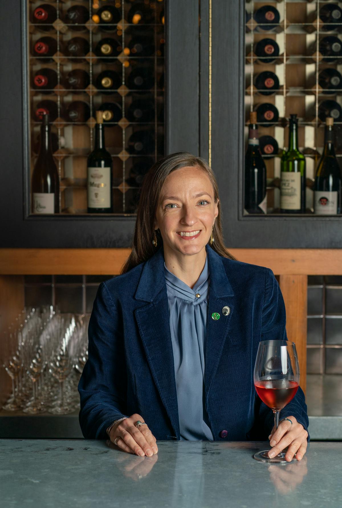 a person sitting at a table with wine glasses and smiling at the camera
