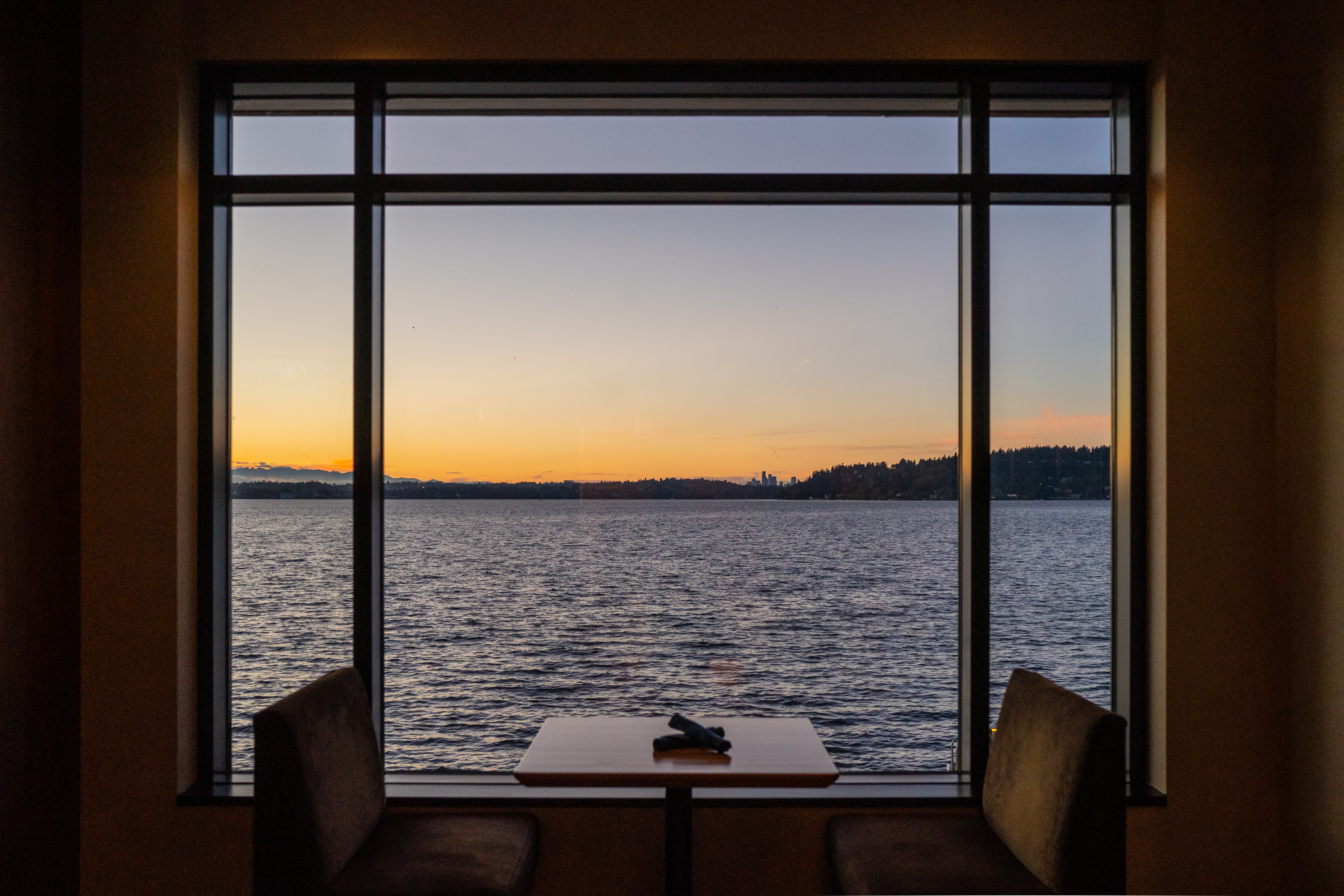 Table for two sitting in front of a large window during sunset featuring Lake Washington and the Seattle skyline from a distance.