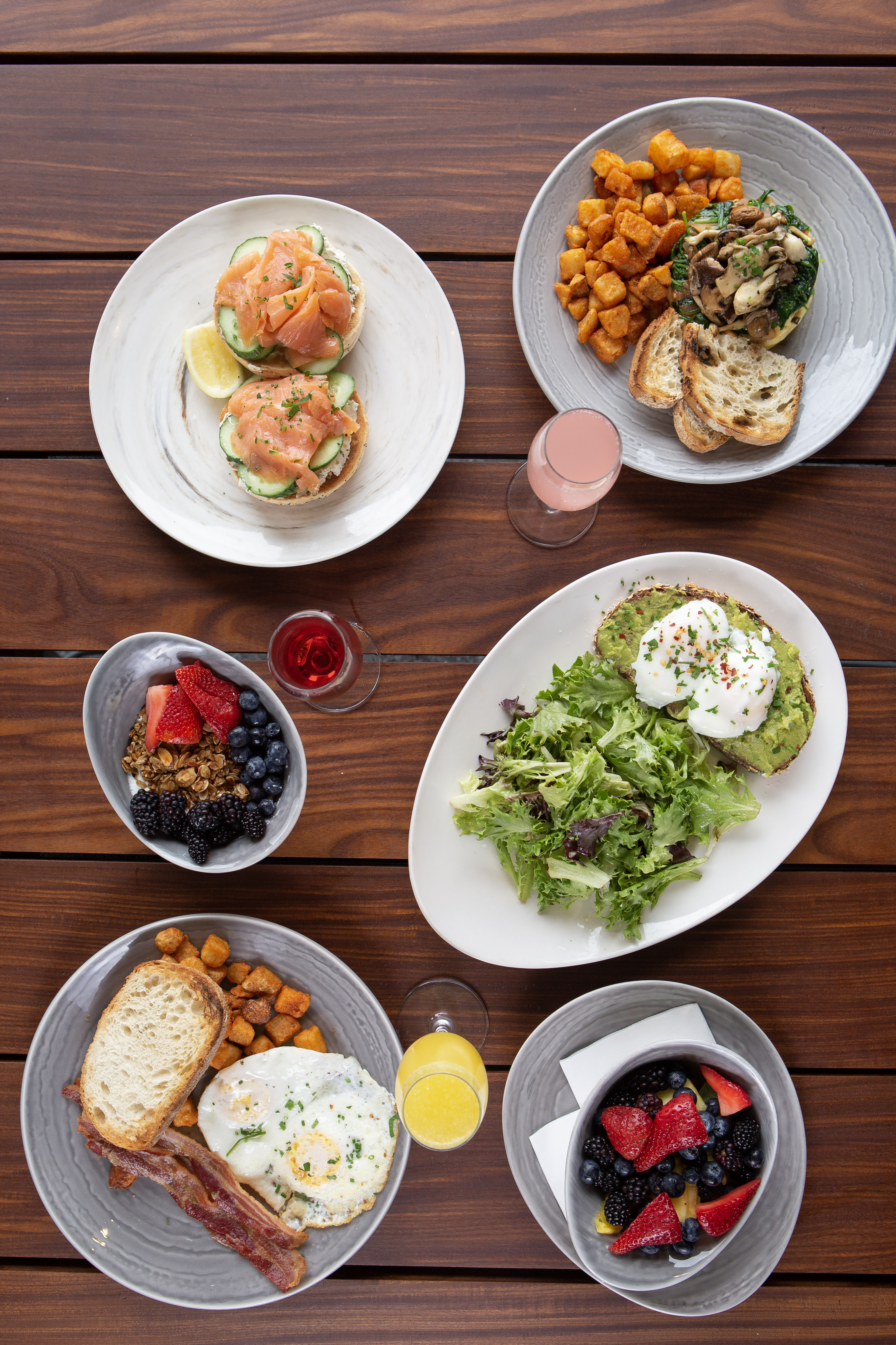 overhead photo of breakfast meals. Salmon locks, mushroom scramble, potatoes, avocado toast, granola, farmers breakfast of eggs, bacon, toast, and fruit bowl.