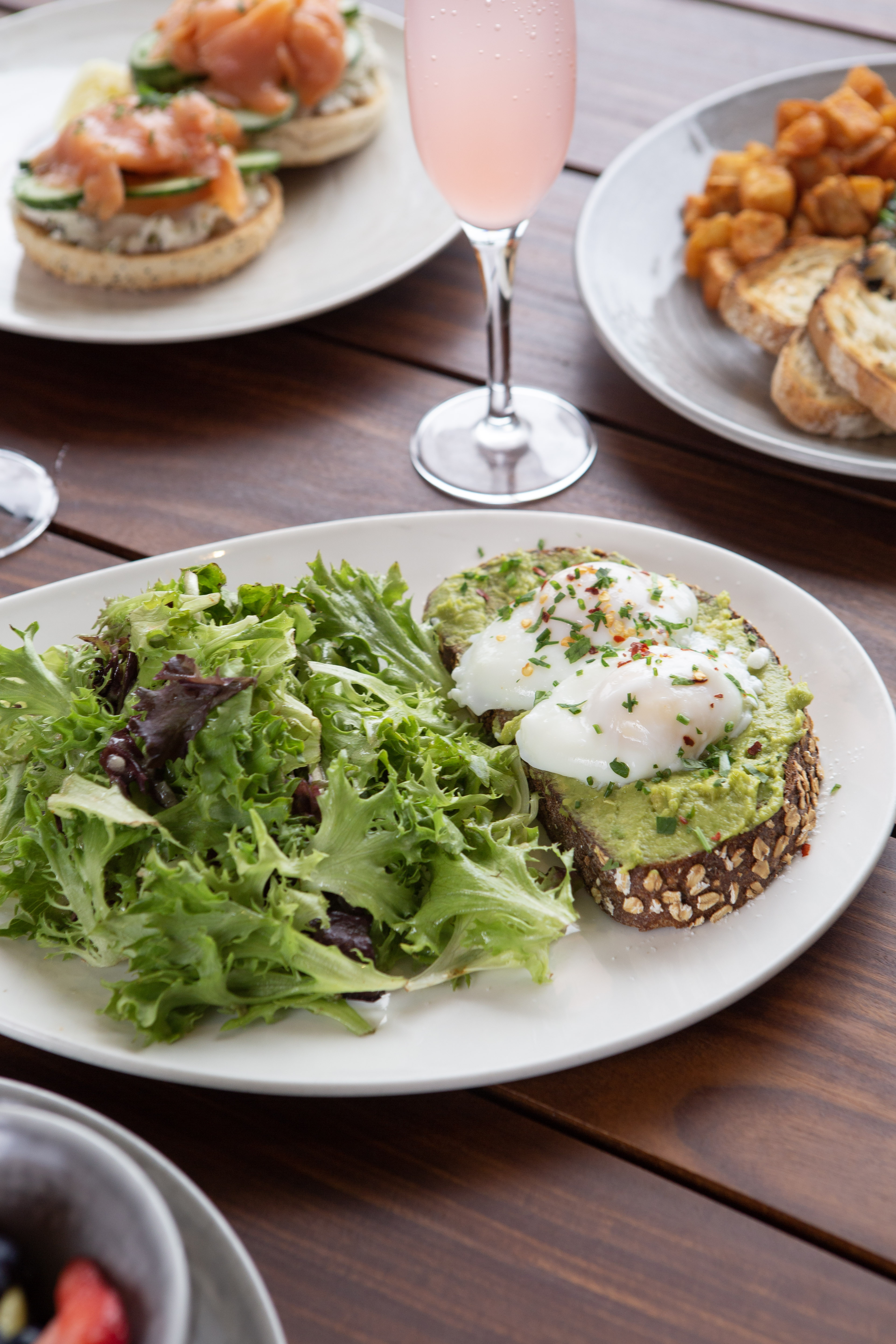 Avocado toast with 2 eggs and side salad. Mimosa in the background and salmon locks and potatoes.