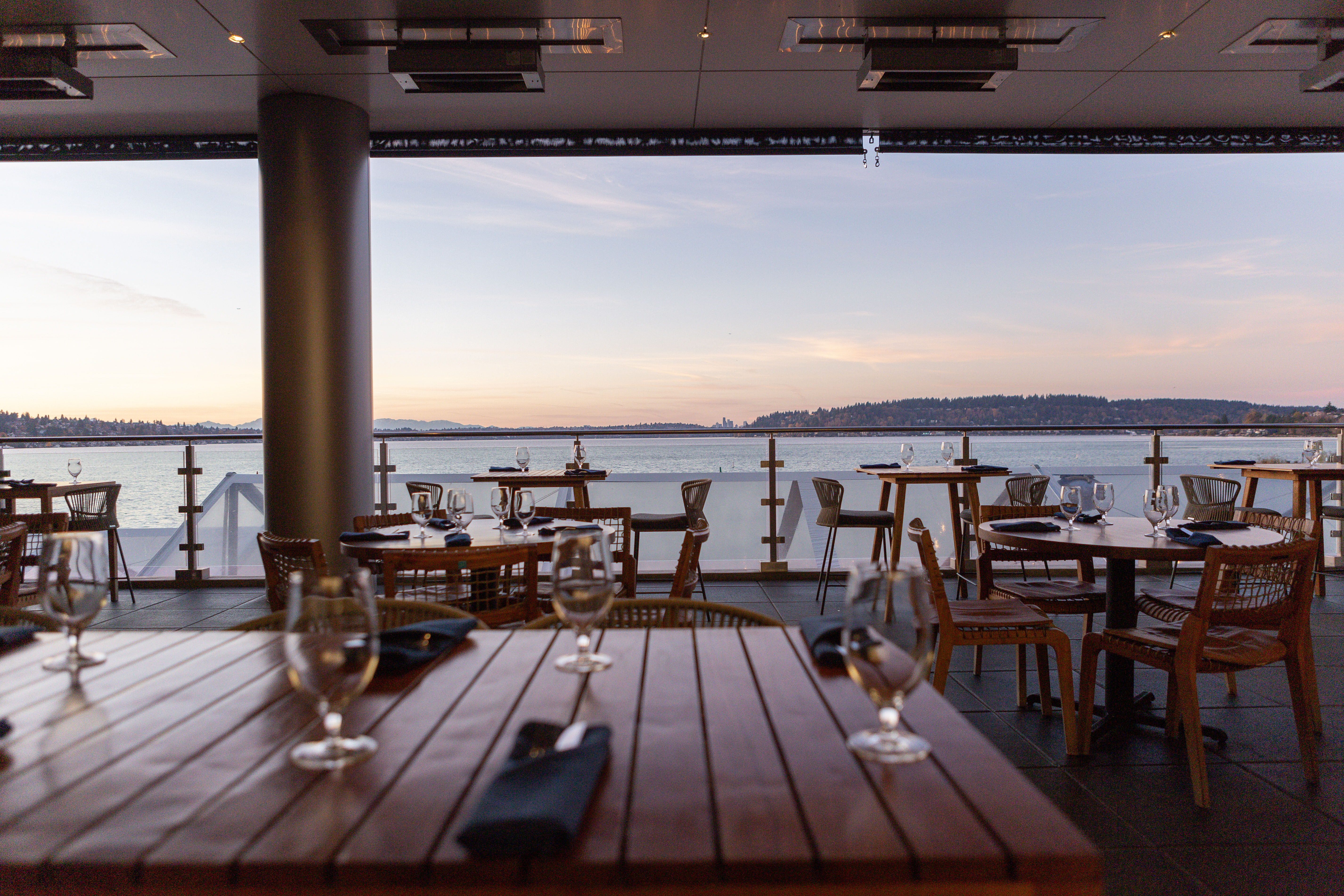 Tables on a patio overlooking Lake Washington at sunset with Seattle skyline in the far view.