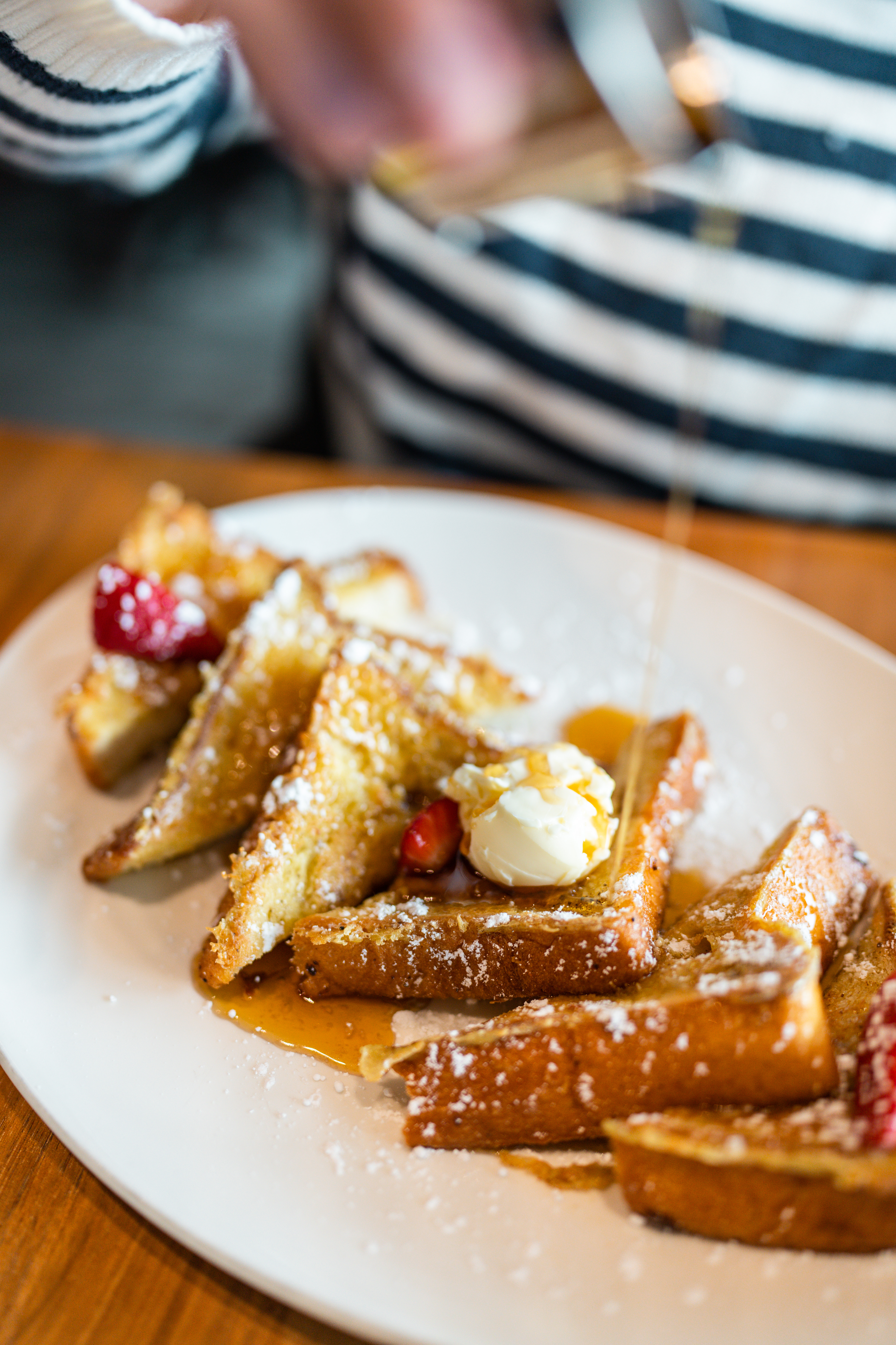 Close up of French toast, butter, powder sugar, and syrup being poured.