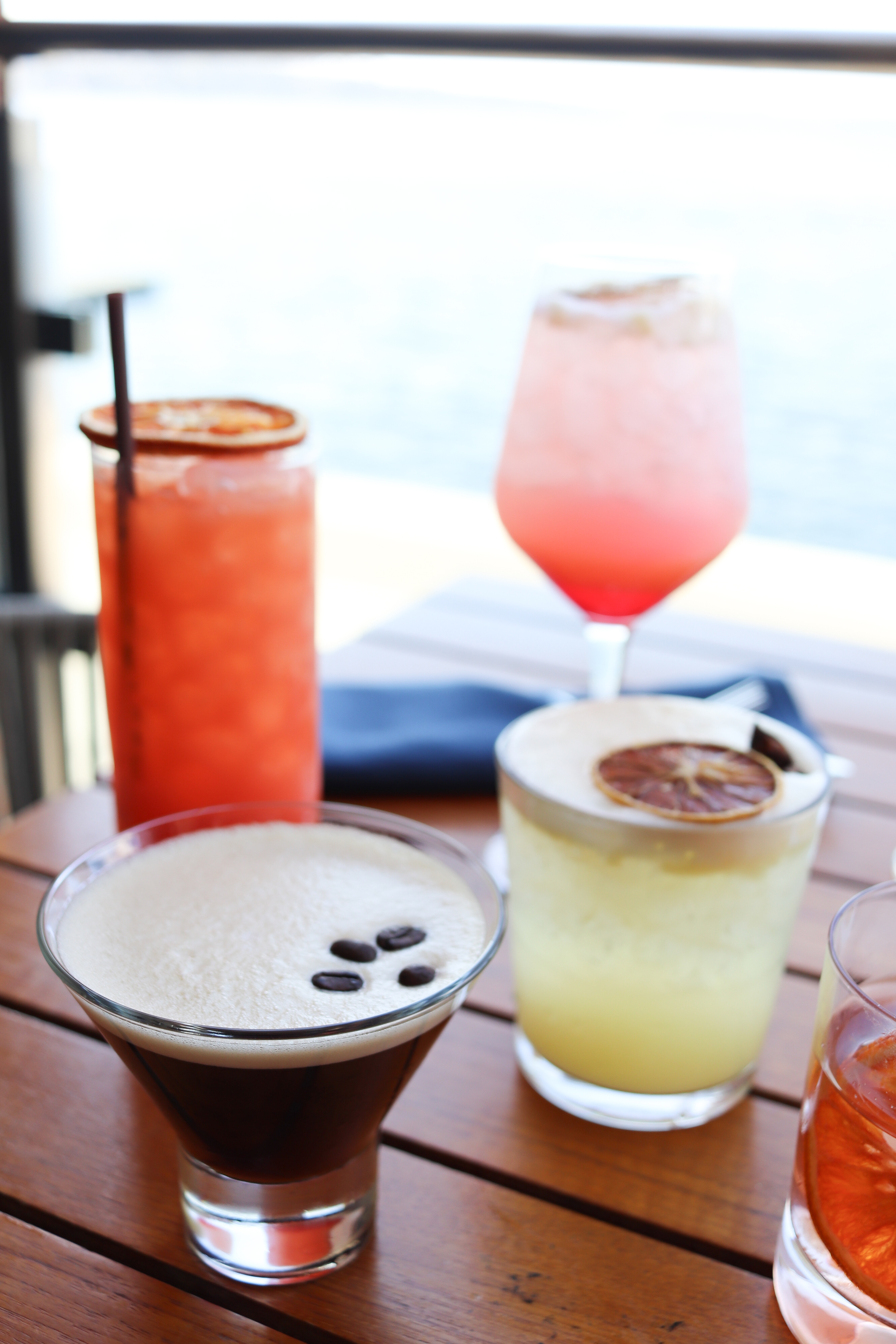 4 cocktails on a table. One orange, one pink, one yellow, one brown.