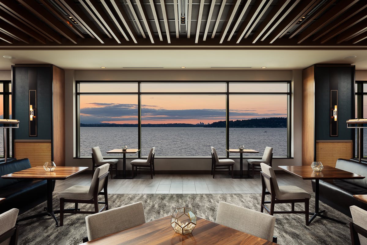 Inside dining room featuring large windows filling the wall with a sunset view of Lake Washington and Seattle in the distance.
