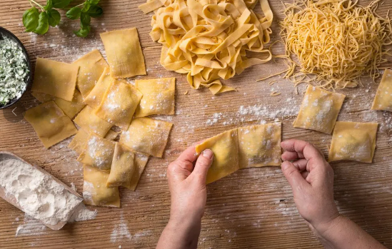 Pasta making on cutting board with different types of pasta & flour.