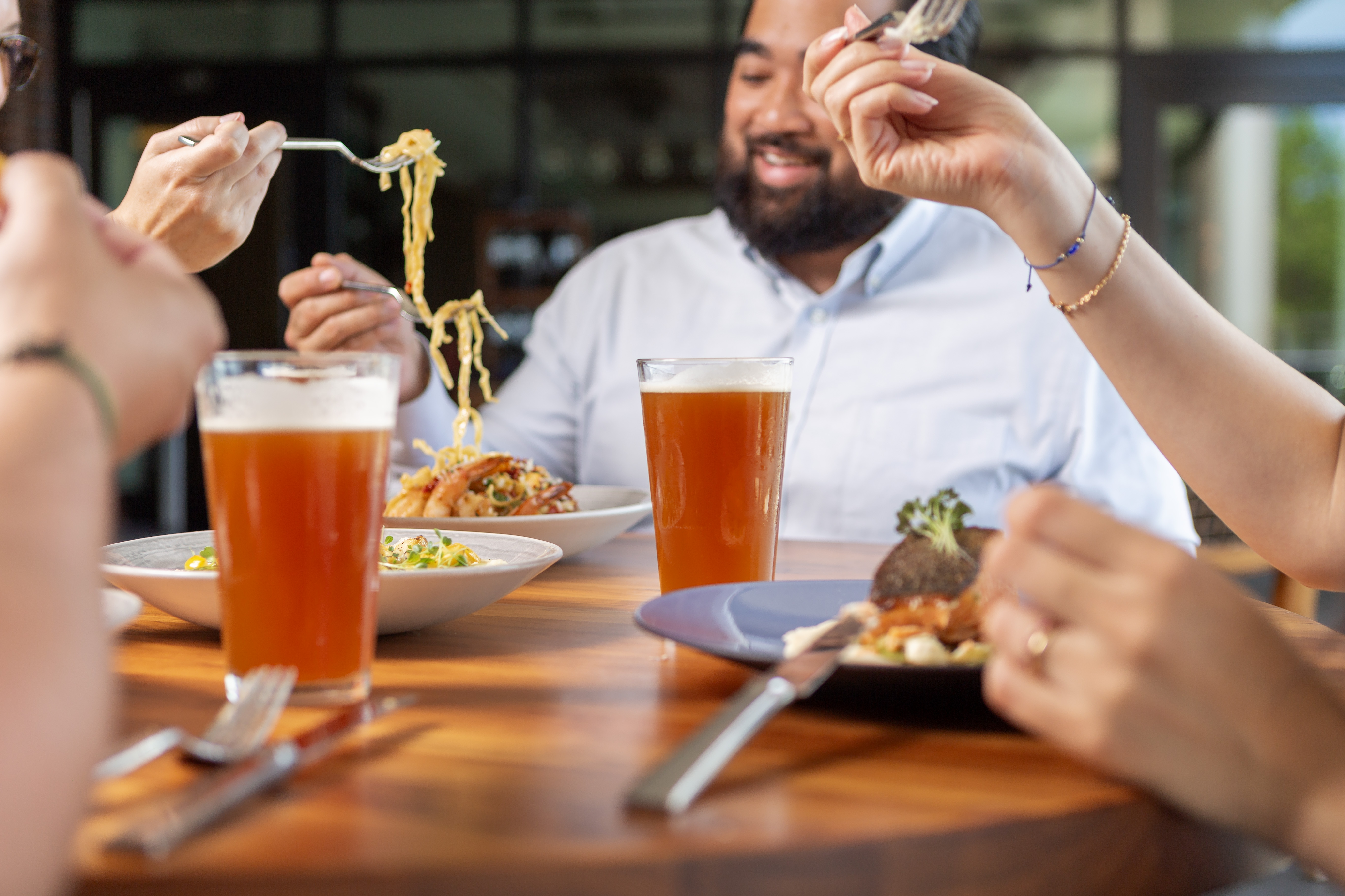group of people eating at a table. Pasta hanging from forks and two beers.