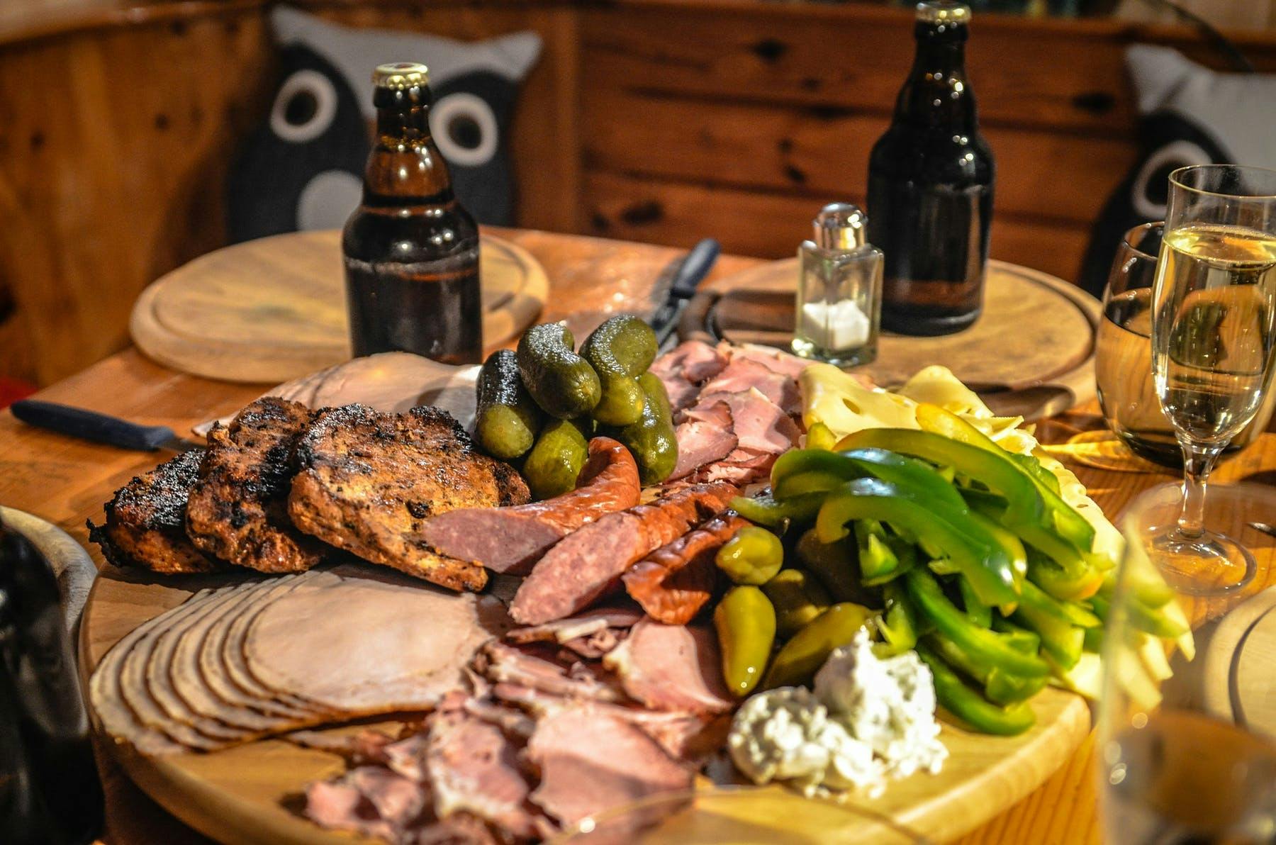 a plate of different types of meat, green pepper, cheese, jalapeño and pickles on a table